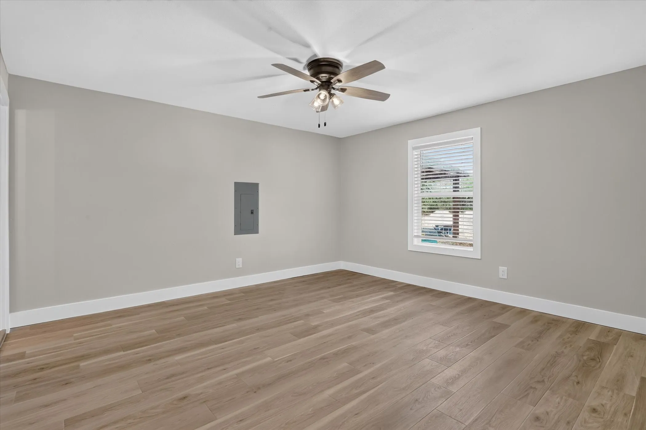 Neutral gray walls with white trim, wood-finish flooring, and a ceiling fan with integrated lighting