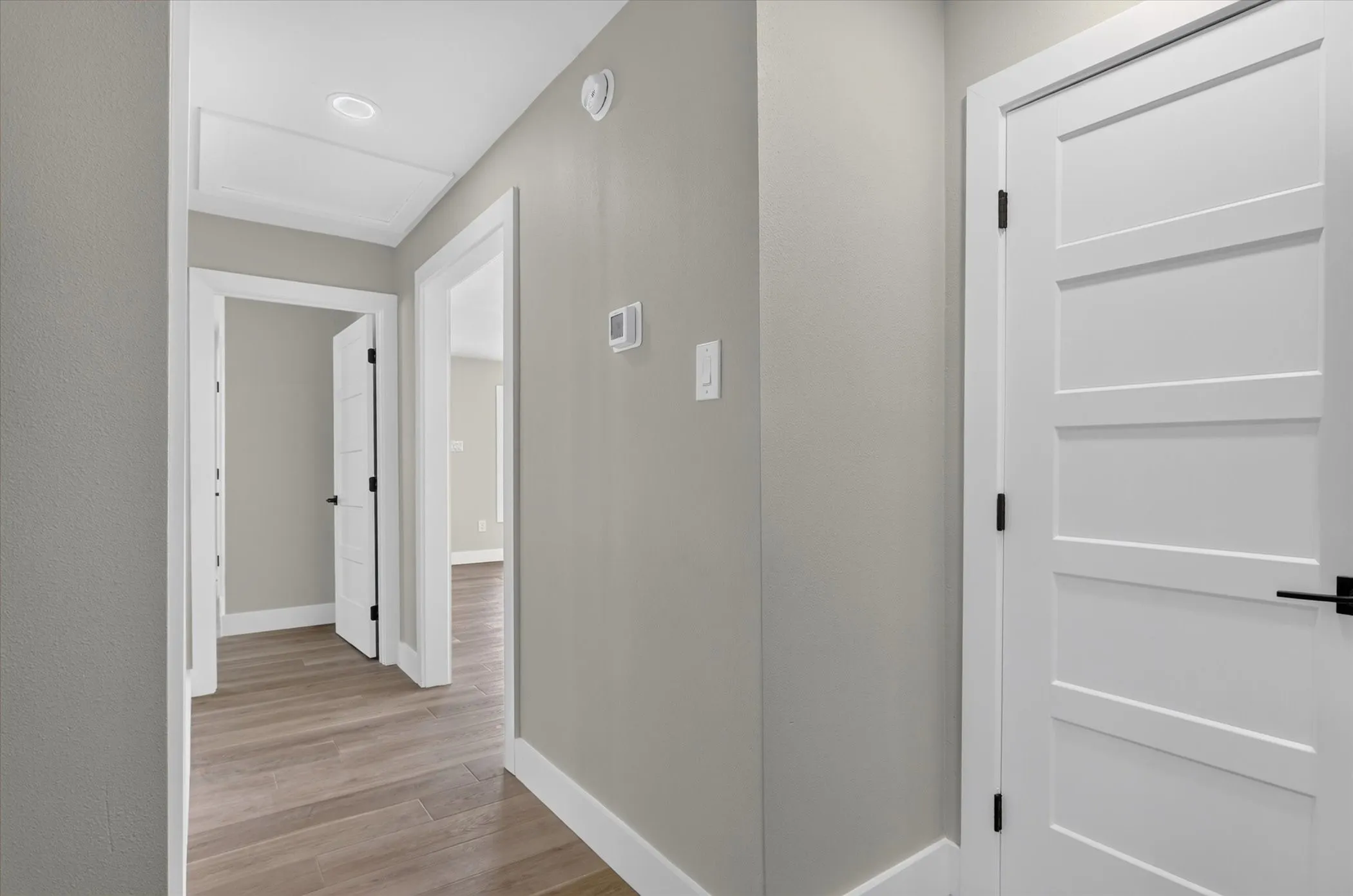 Hallway featuring wood-finish flooring, white trim, recessed ceiling lighting, and solid white doors with matte black hardware