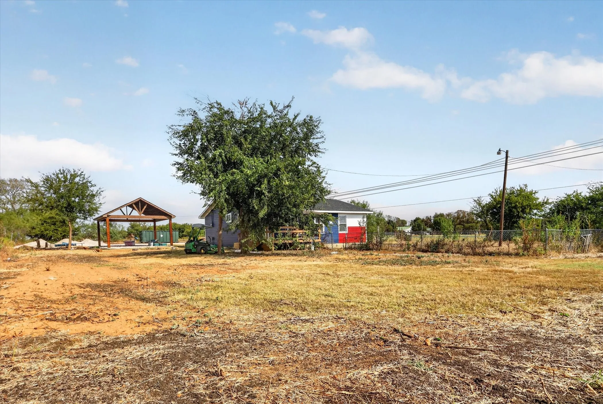 Expansive lot featuring a detached covered patio structure, mature trees, and a separate outbuilding