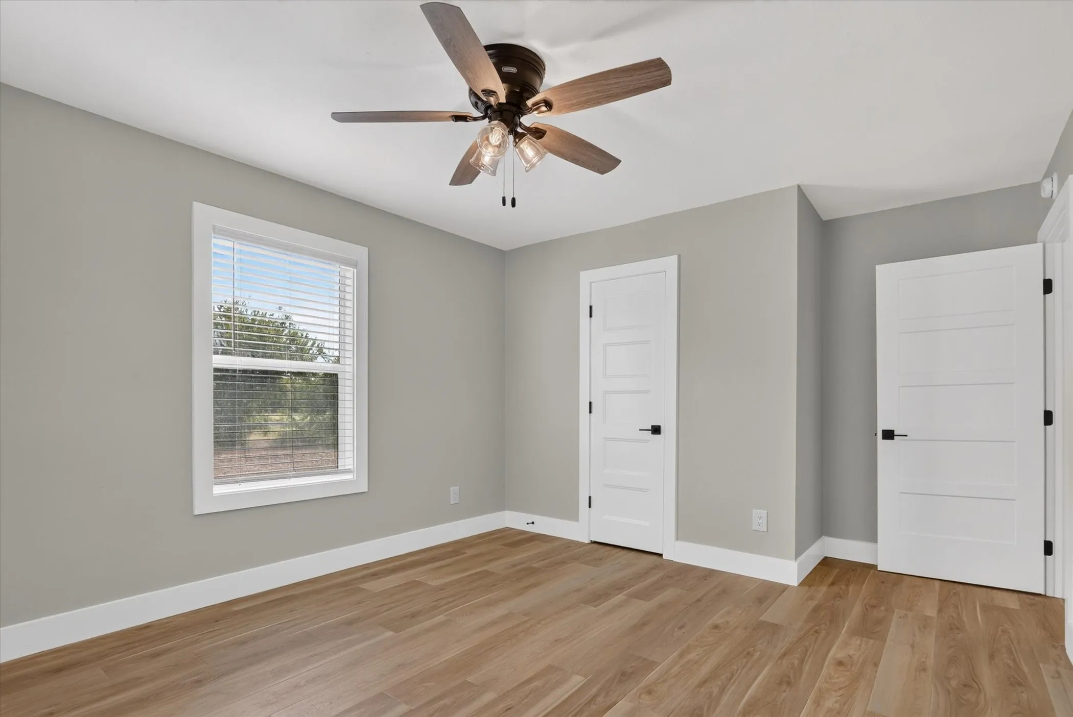 Wood-finish flooring, white trim, a modern ceiling fan with lighting, a window with blinds, and paneled interior doors