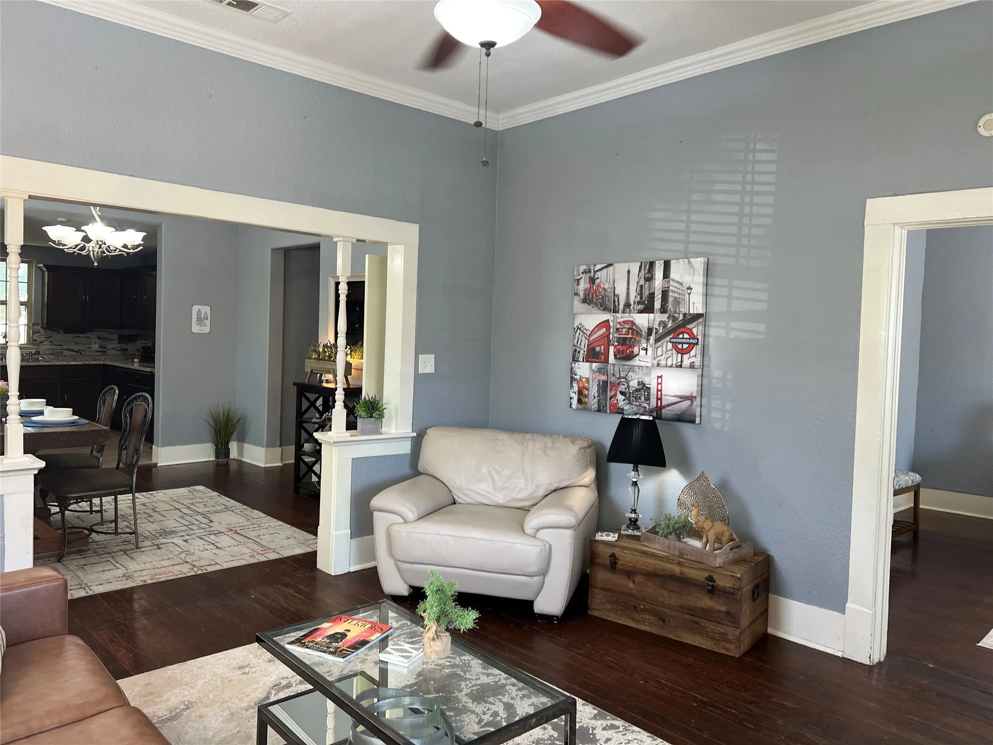 Hardwood flooring, painted walls, crown molding, ceiling fan, and built-in architectural columns with trim