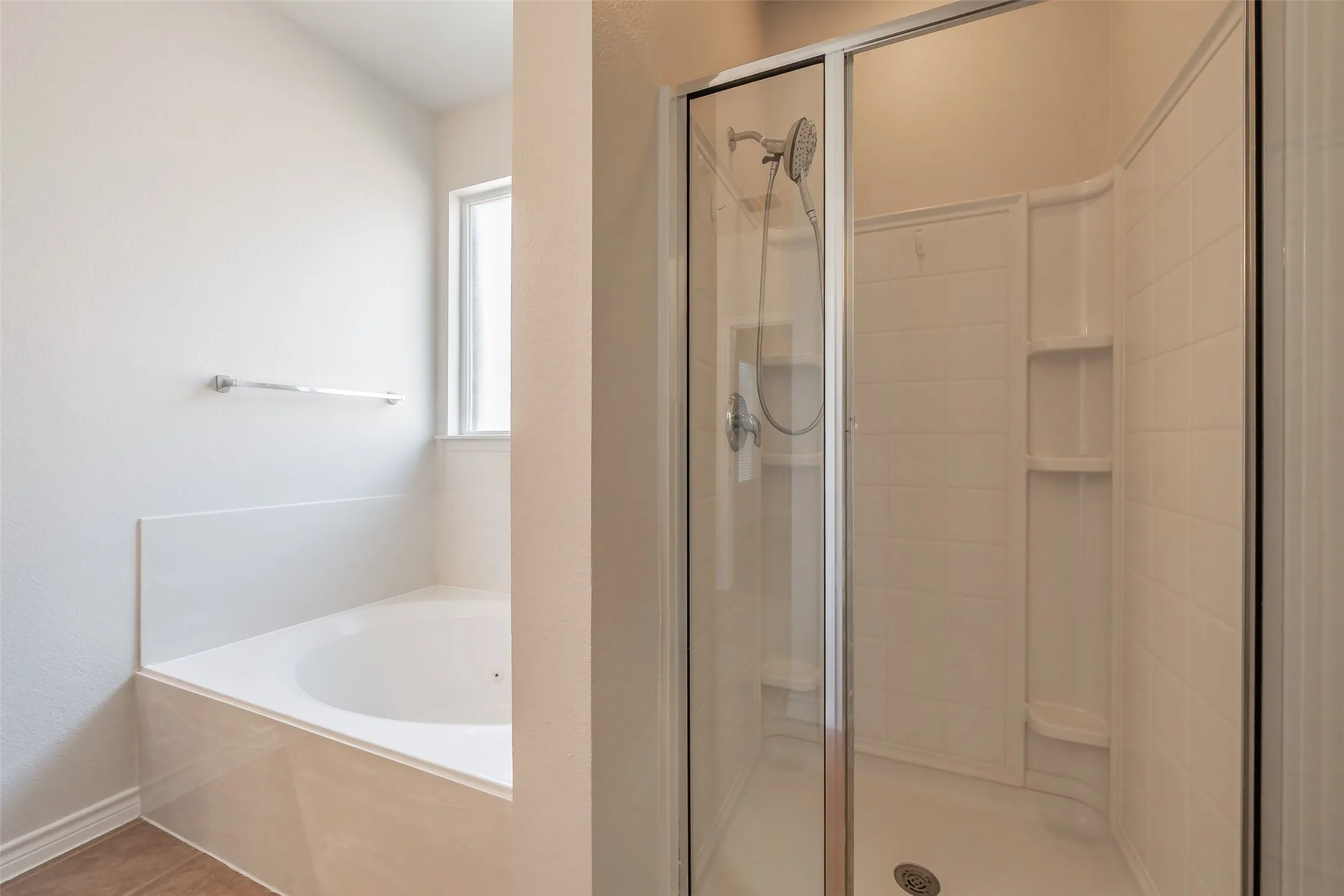Built-in bathtub with tiled surround, adjacent to a shower with a clear glass enclosure and integrated shelving