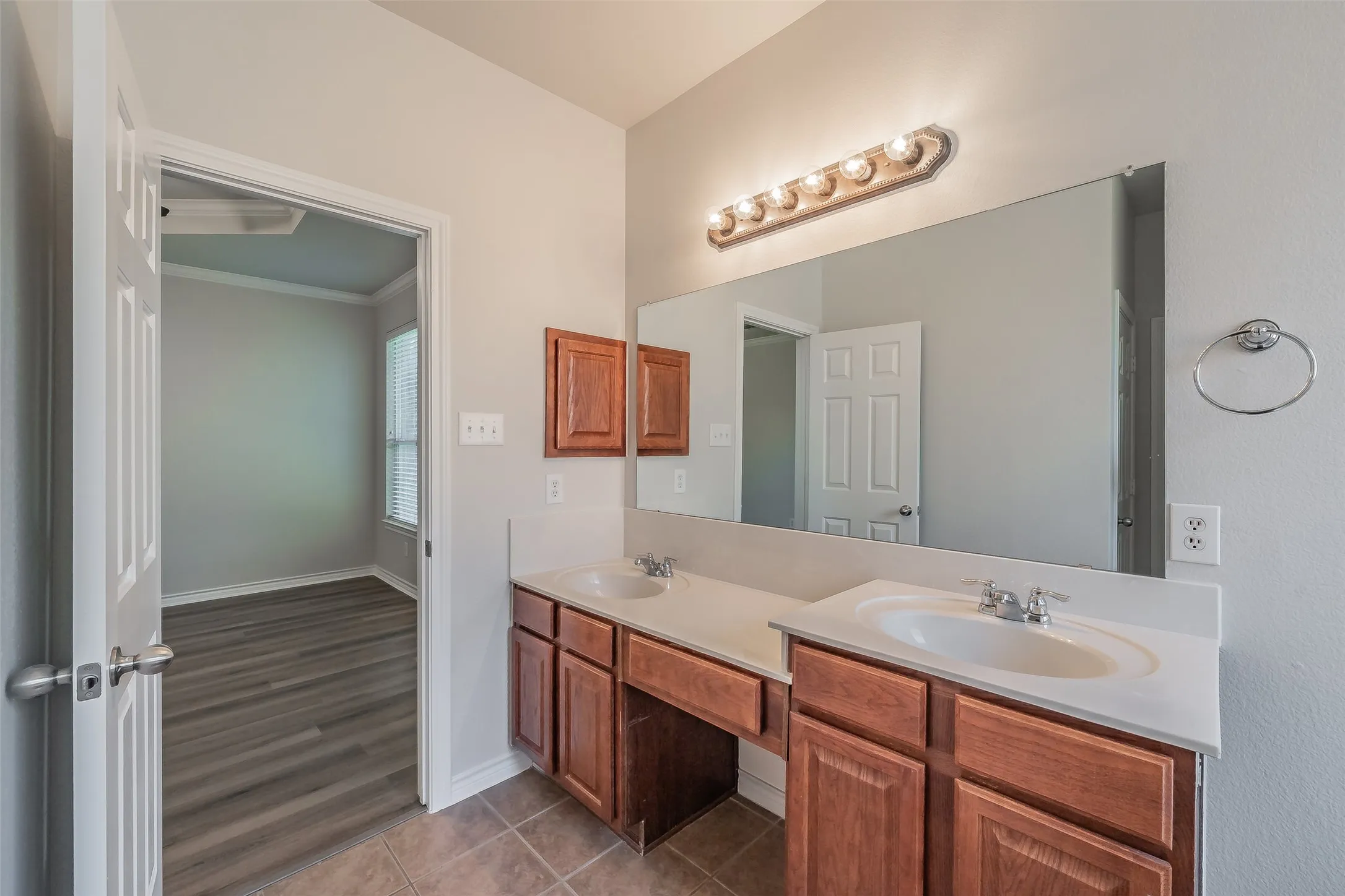 Double vanity with integrated sinks, expansive wall-mounted mirror, and warm wood-finish cabinetry