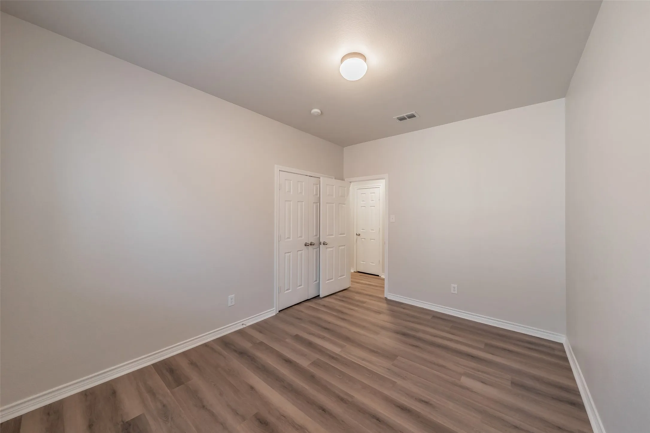 Wood-finish flooring, white walls, flush mount ceiling light, and white paneled doors