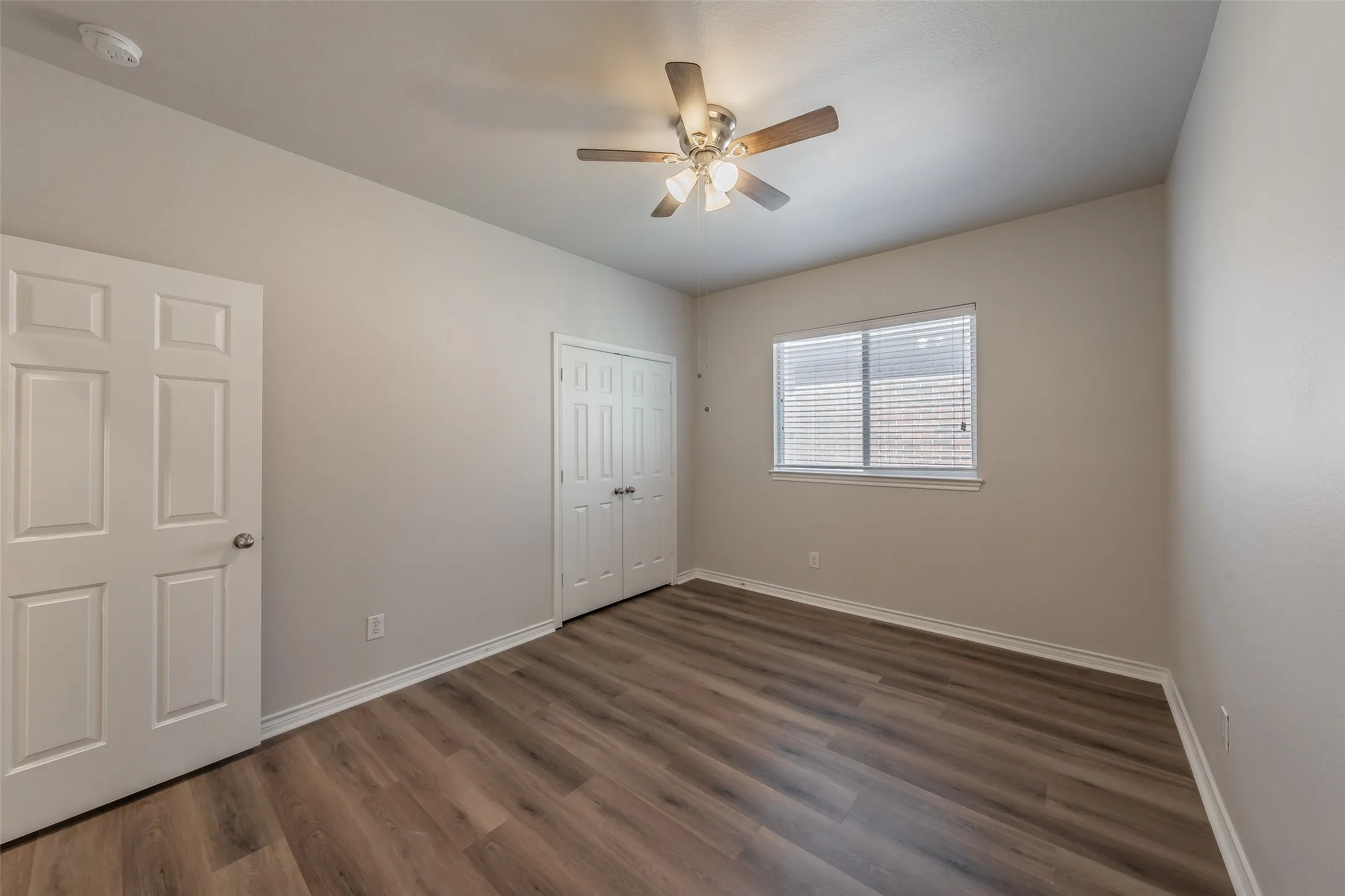 Wood-finish flooring, ceiling fan with integrated lighting, window with blinds, and bi-fold closet doors