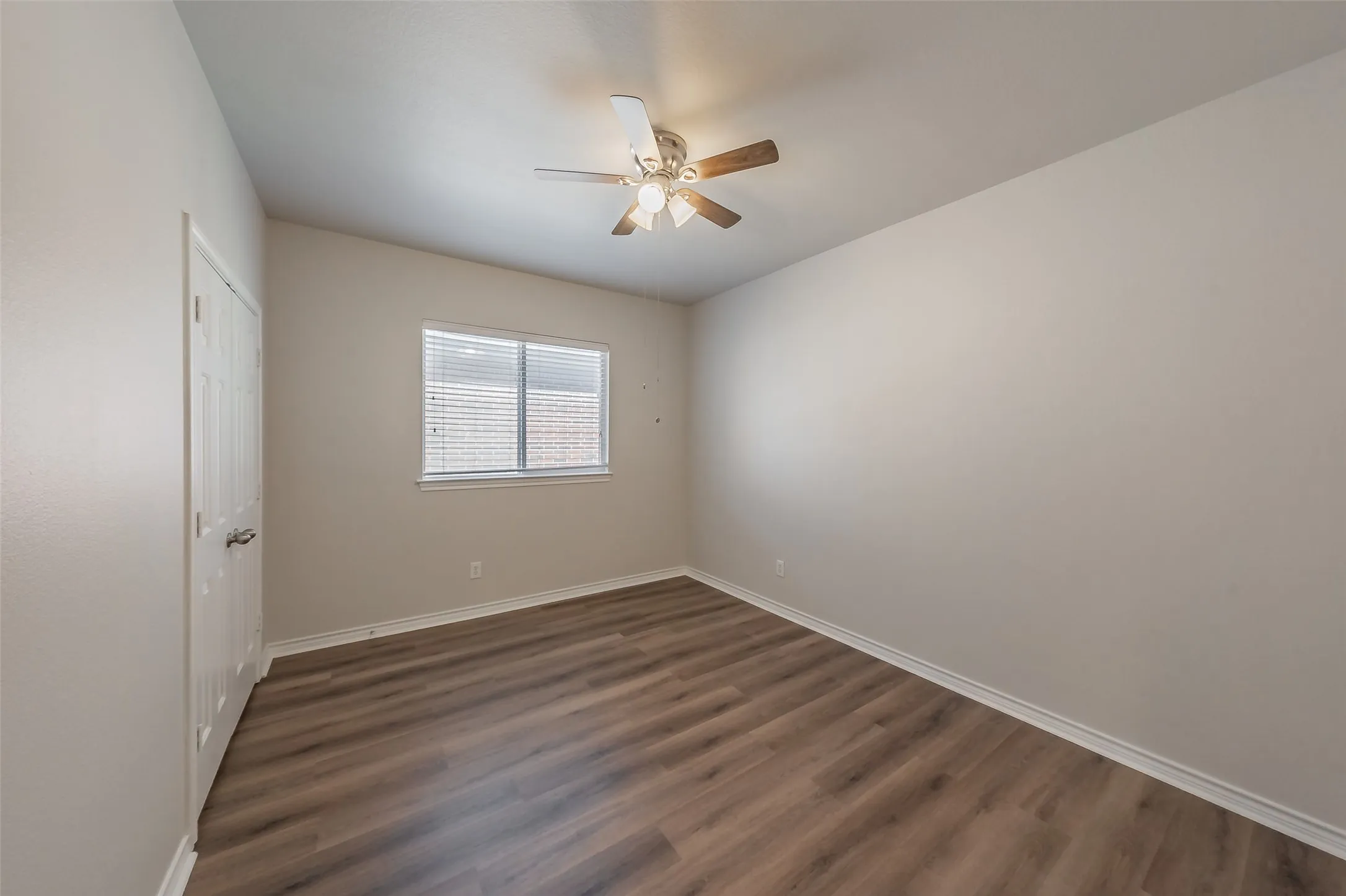Wood-finish flooring, neutral wall tones, window with blinds, white trim, and ceiling fan with integrated lighting