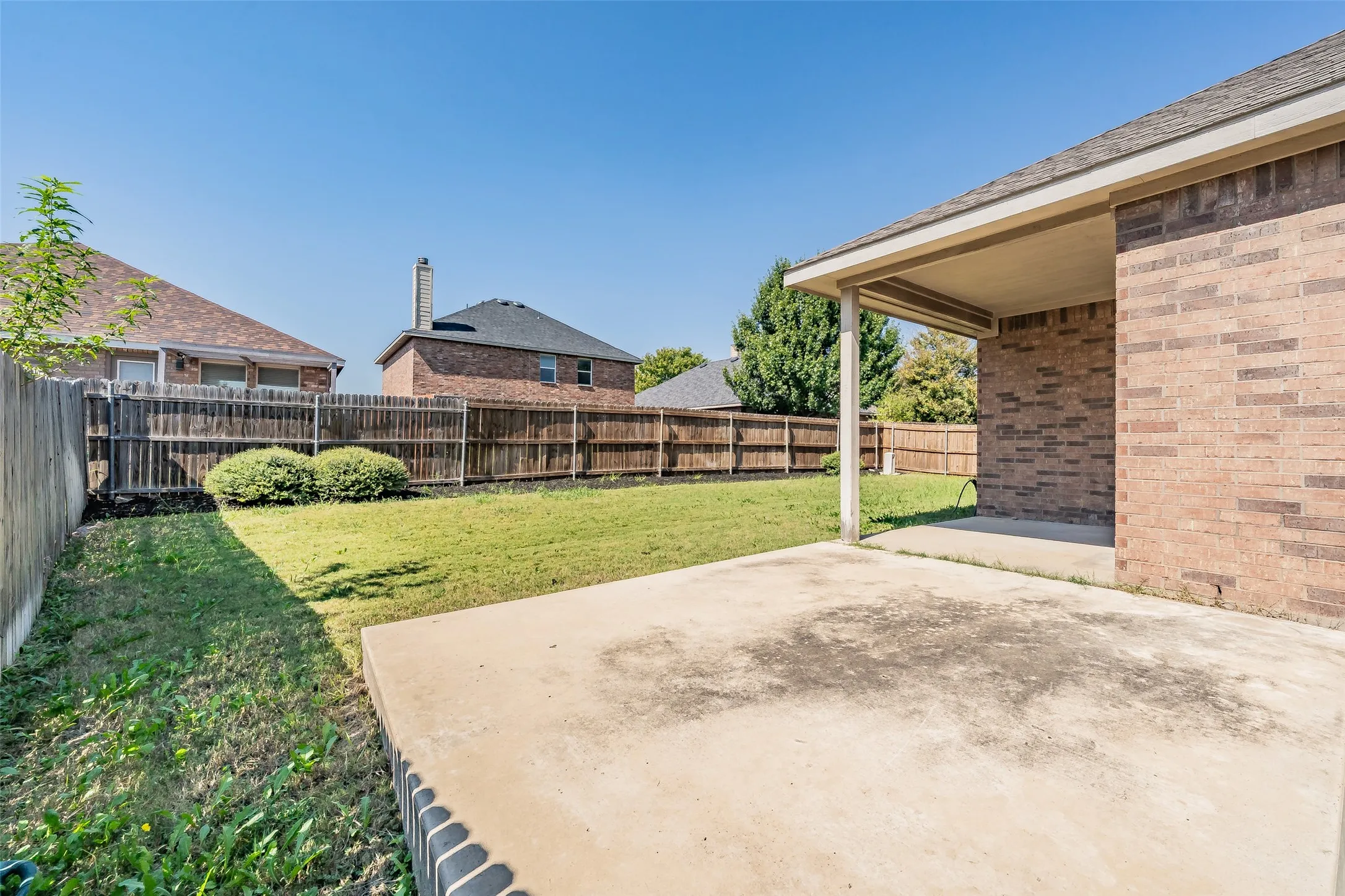 Expansive grassy backyard featuring a wood fence, concrete patio, and covered porch area