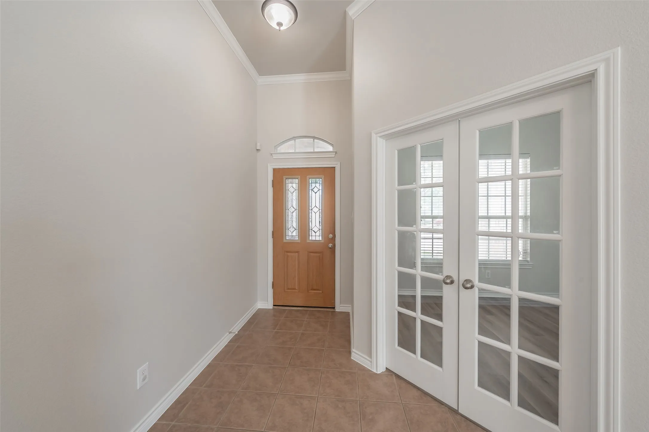 Entryway featuring tiled flooring, a wooden front door with decorative glass inserts, an arched transom window, and white French doors with glass panels