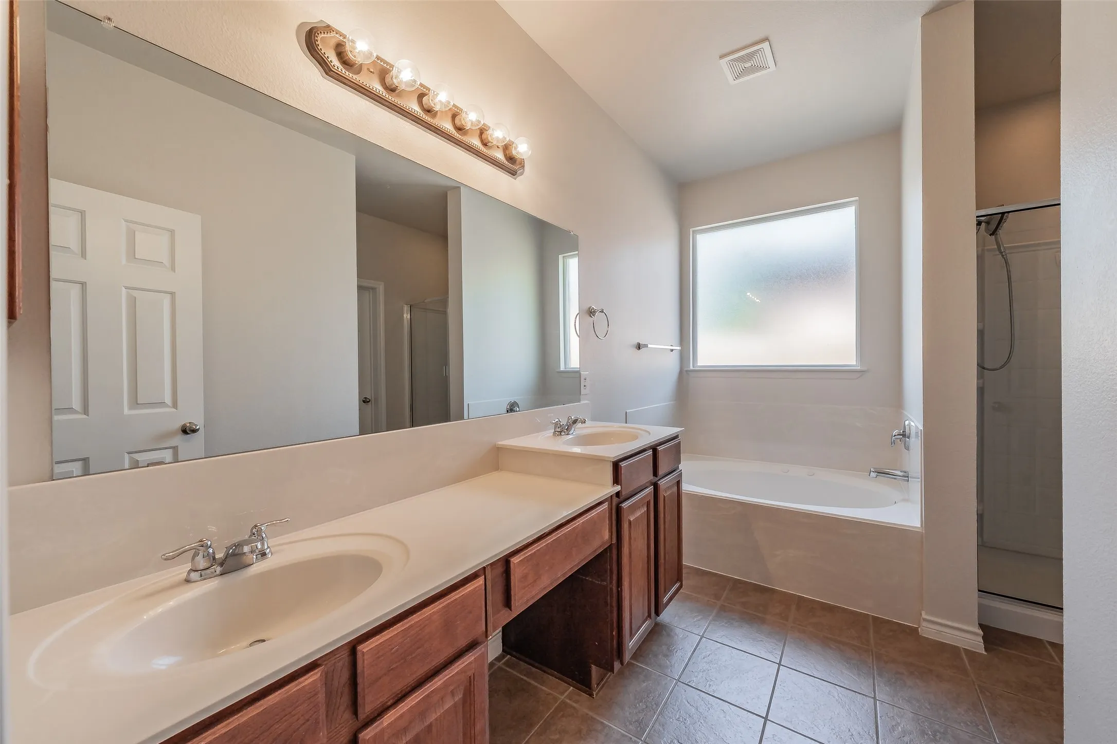 Dual undermount sinks with chrome fixtures, wood-finish cabinetry, built-in bathtub, and a separate shower enclosure