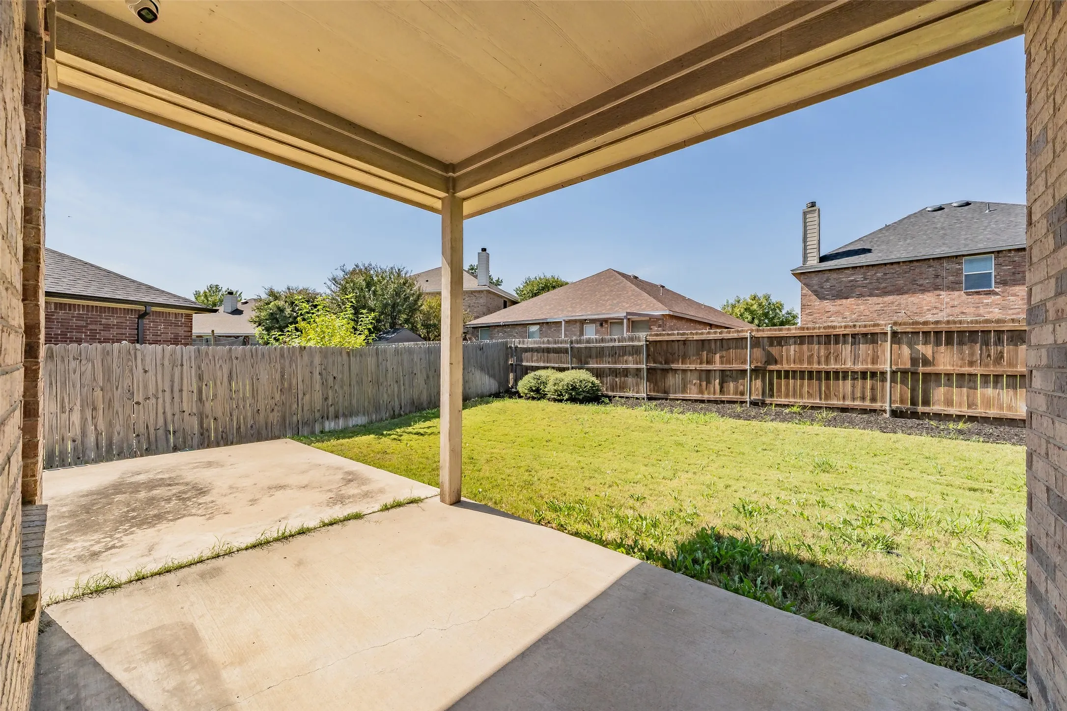 Covered patio with a concrete slab, overlooking a fenced backyard with a grass lawn