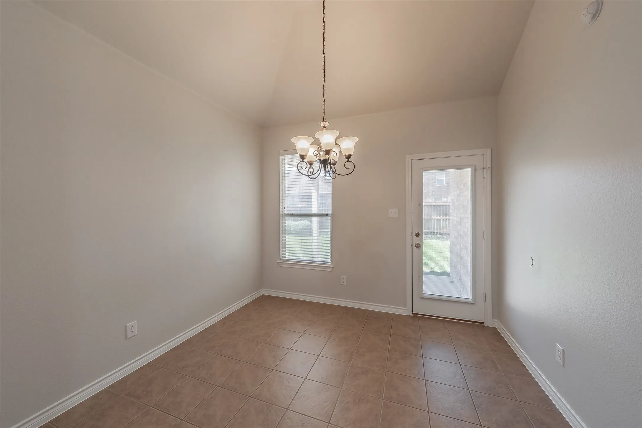 Vaulted ceiling with an elegant chandelier, tiled flooring, window with blinds, and a glass-paneled door to the exterior