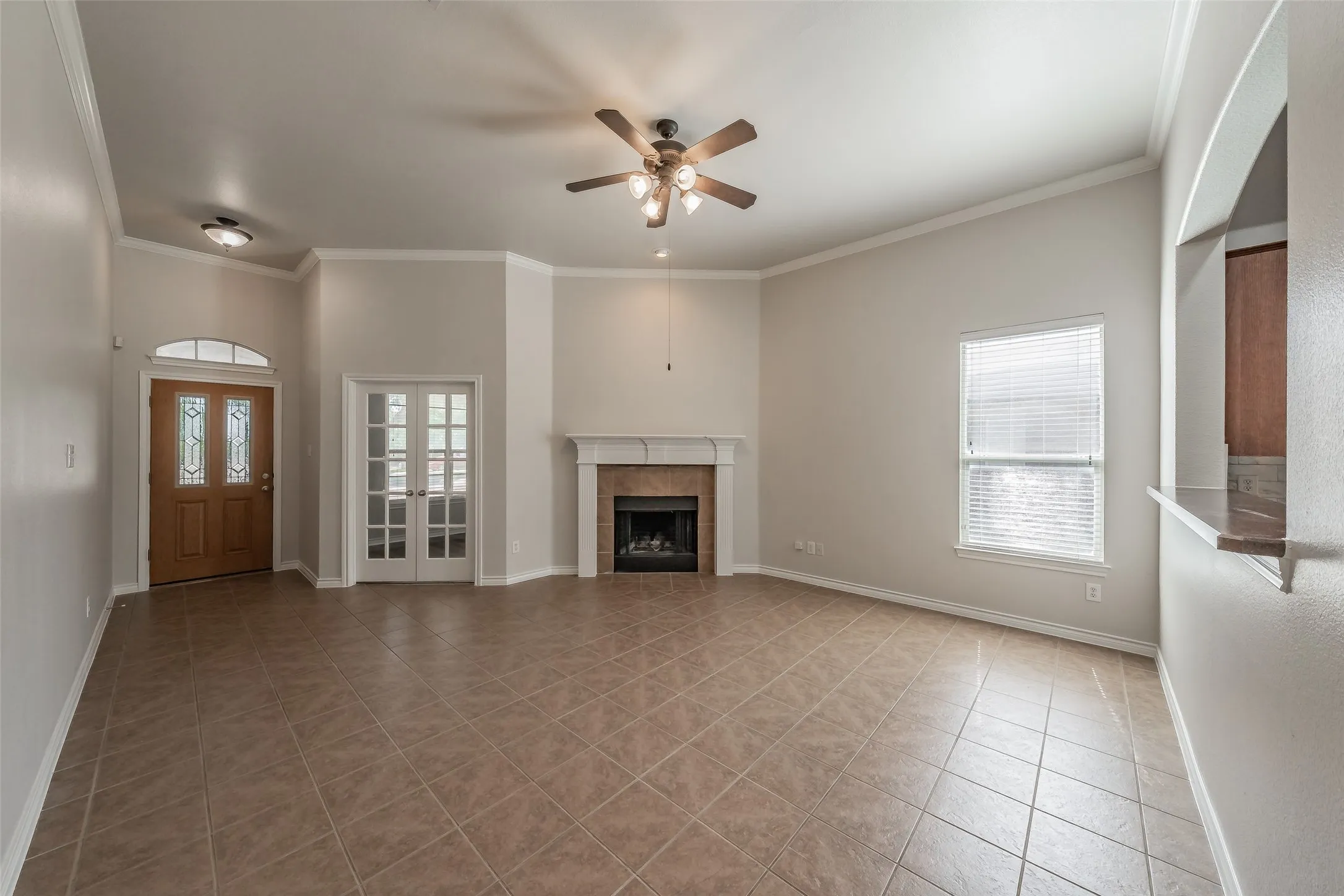 Spacious living area showcasing neutral wall finishes, a ceiling fan with integrated lighting, a wood-burning fireplace with surround, and diagonal-pattern tile flooring