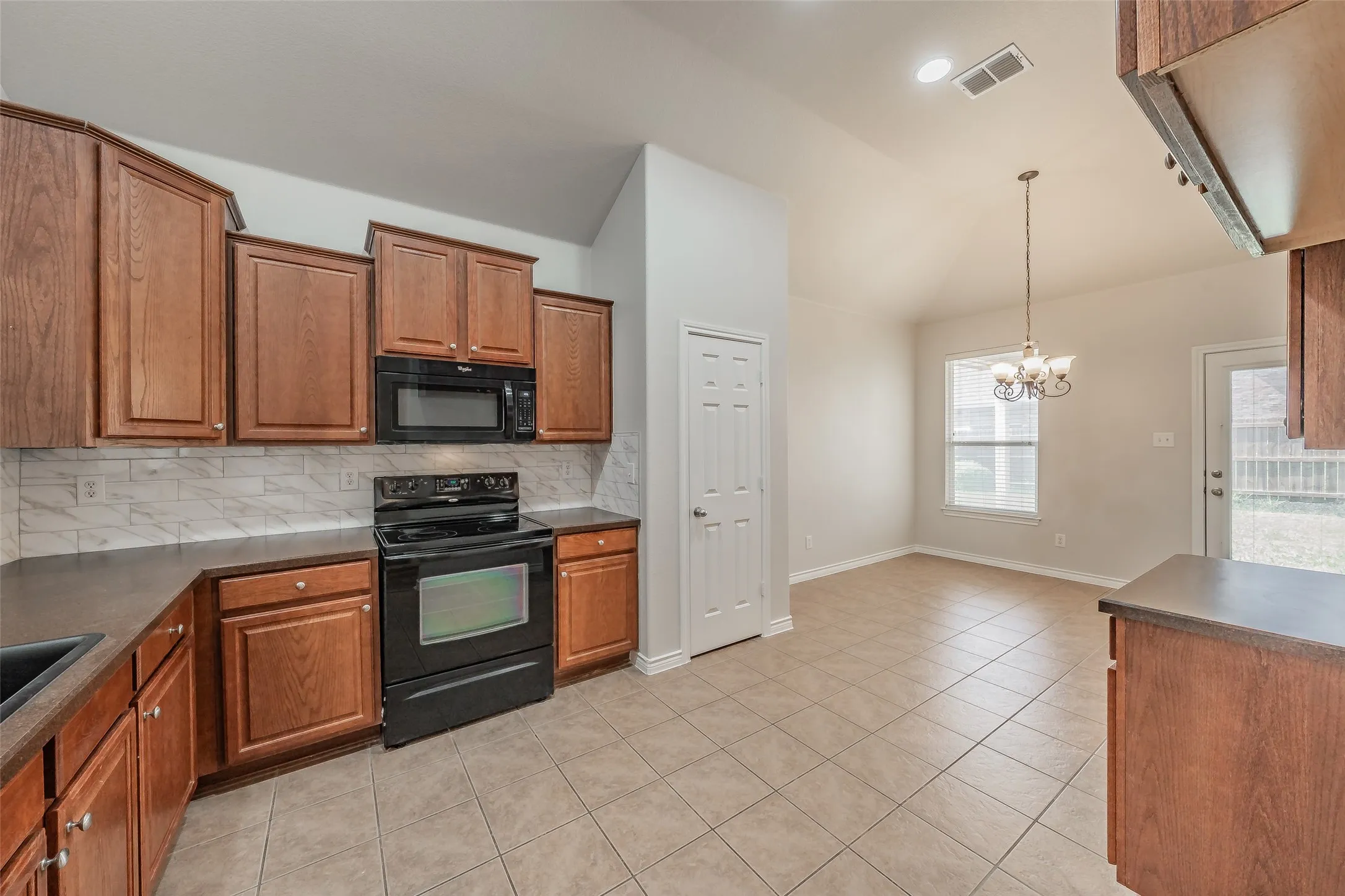 Kitchen featuring wood cabinetry, dark countertops, black appliances, and a tiled backsplash