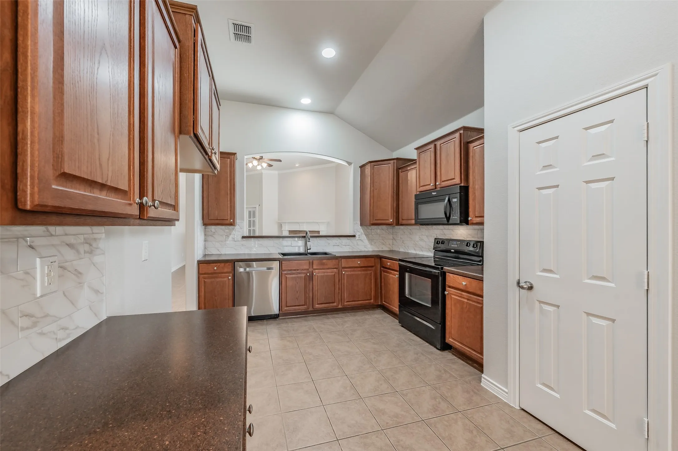 Kitchen featuring wood cabinetry, stainless steel dishwasher, black range, black microwave, and tile flooring