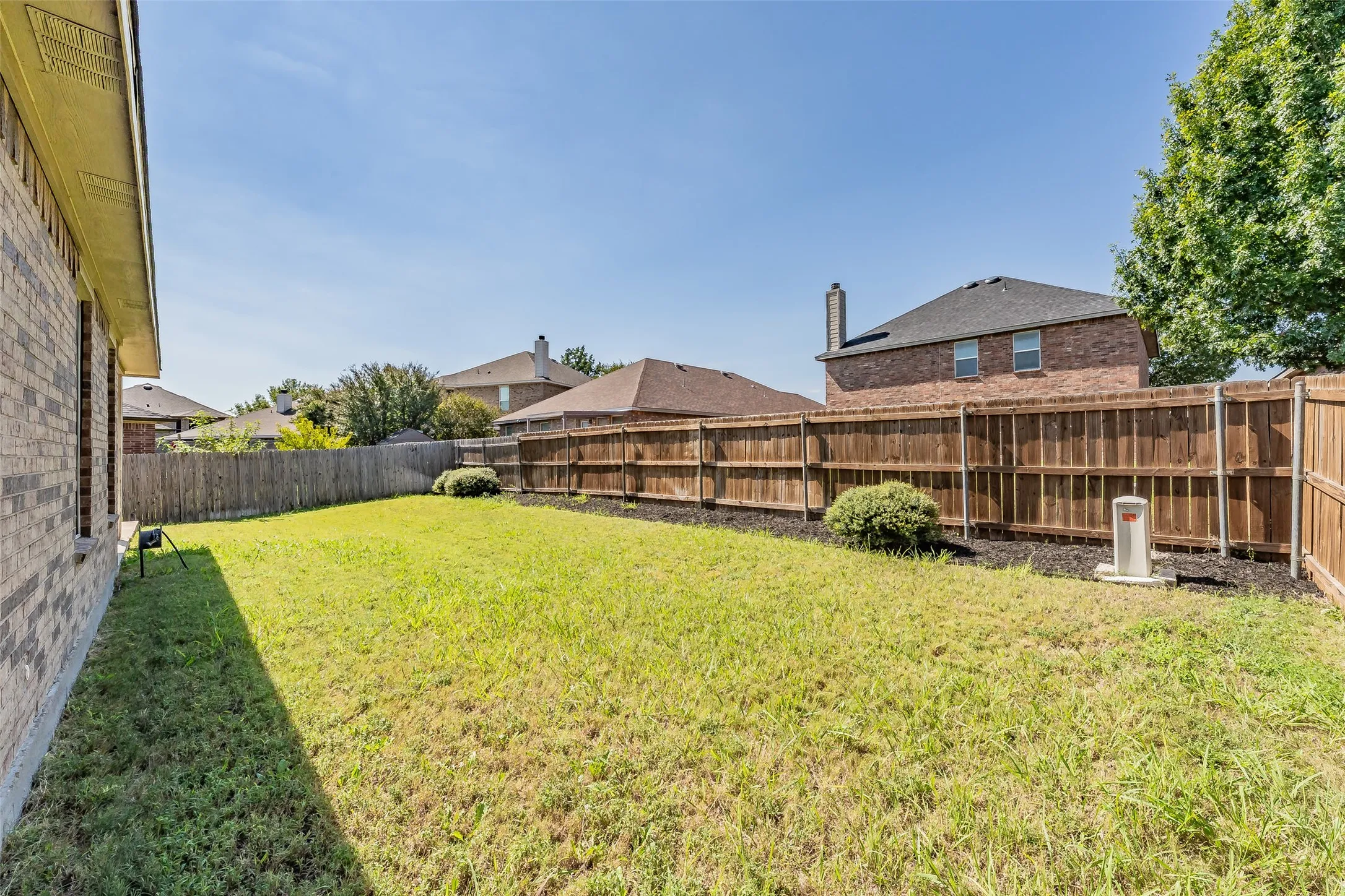 Expansive backyard featuring a wood fence, established landscaping, and a brick exterior