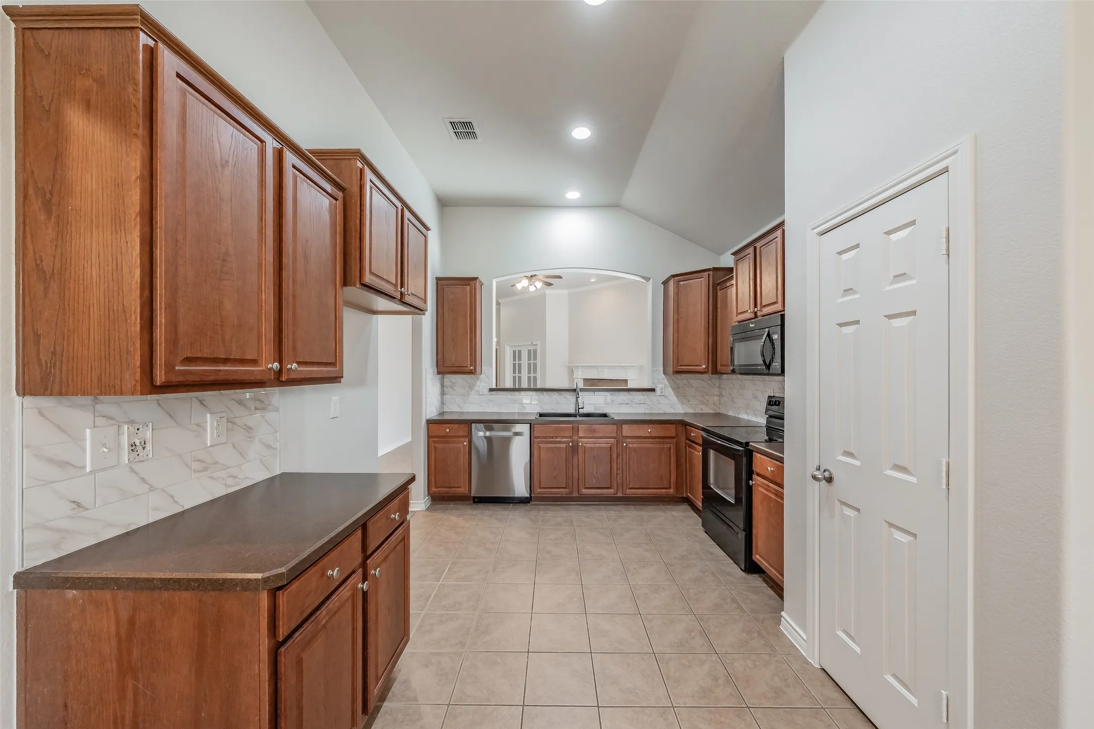 Kitchen featuring wood cabinetry, integrated appliances, ceramic tile flooring, and a stone-look backsplash