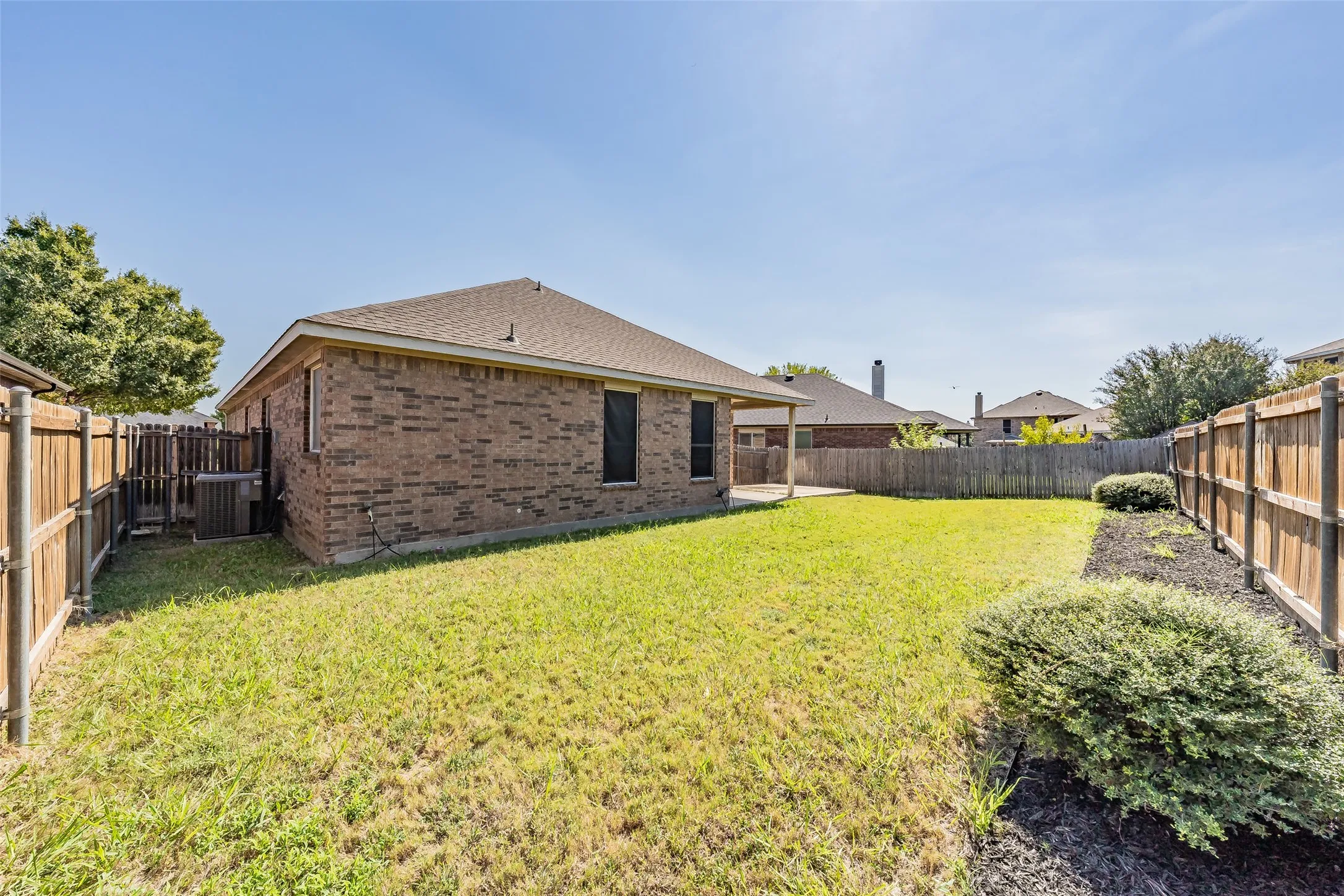Expansive backyard featuring a manicured lawn, brick exterior, covered patio, and wood privacy fencing