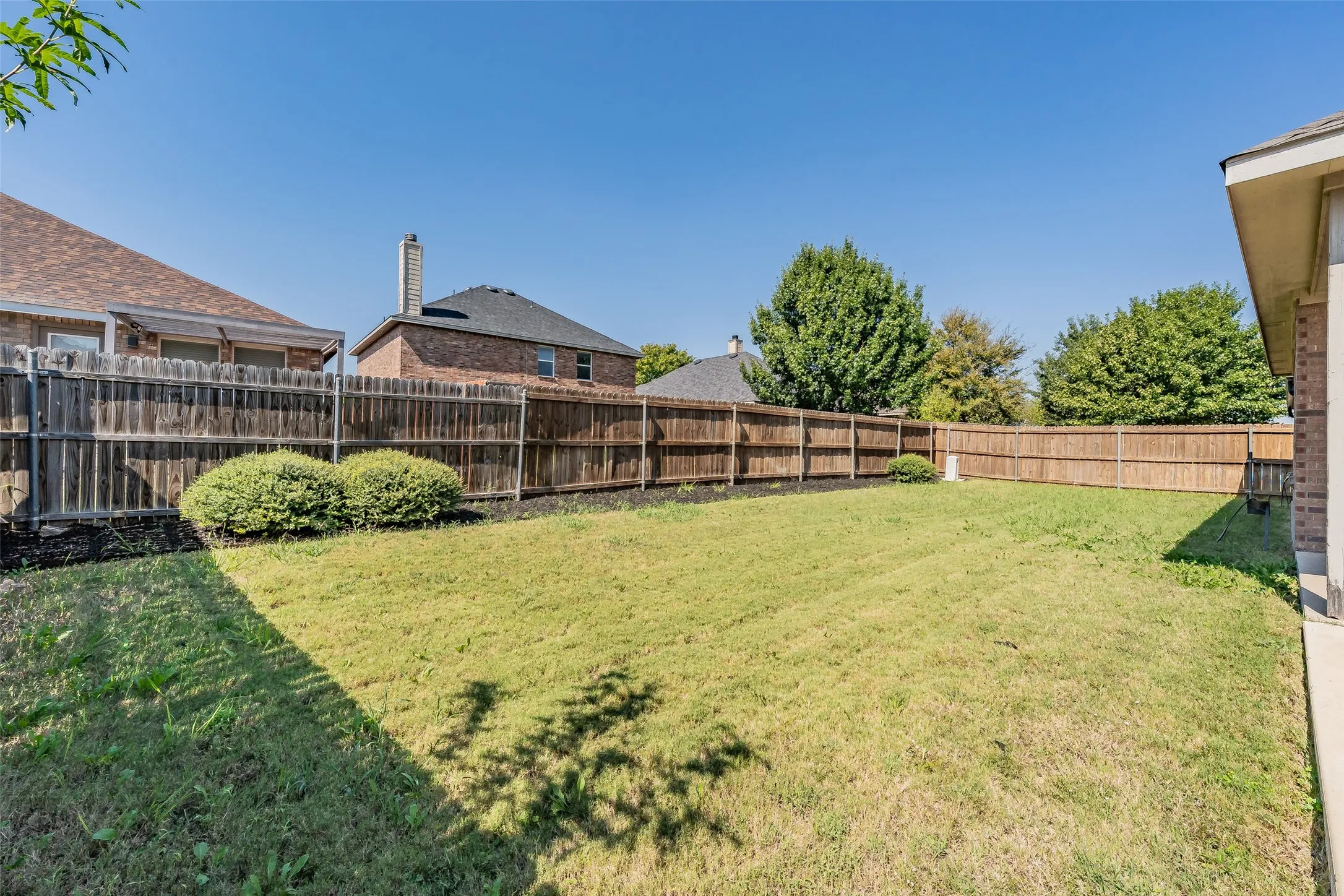 Expansive yard featuring a wooden privacy fence, manicured lawn, and mature trees
