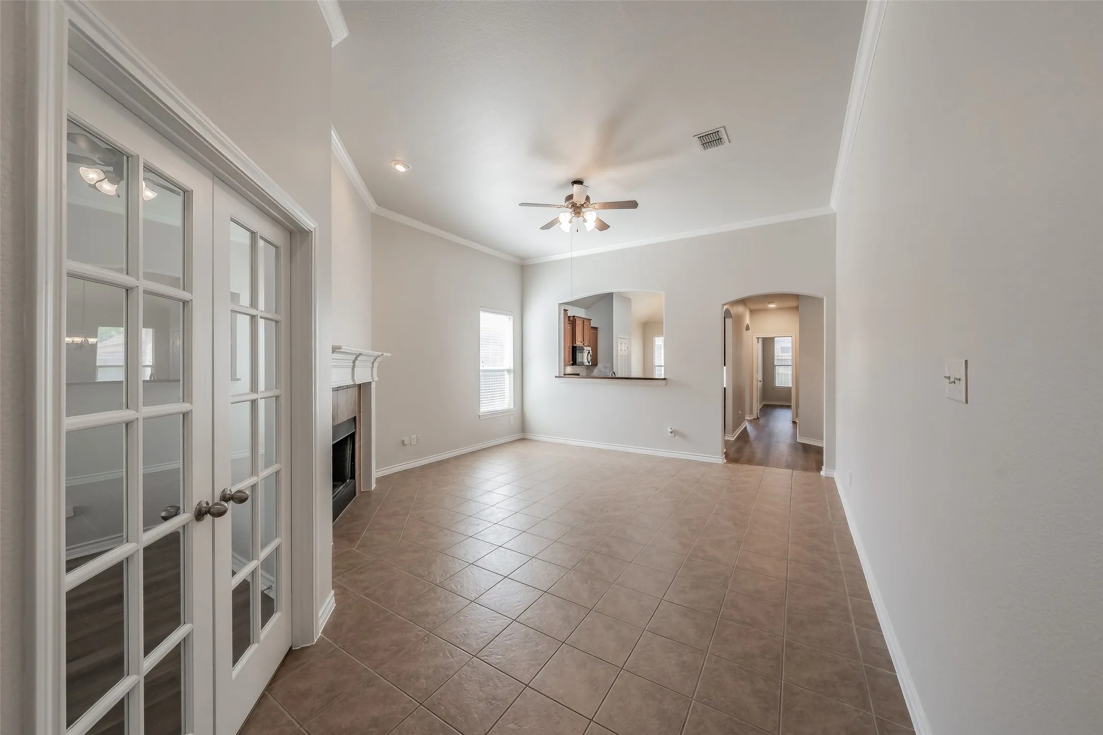 Tile flooring, white French doors, fireplace with mantel, ceiling fan, and arched entryway