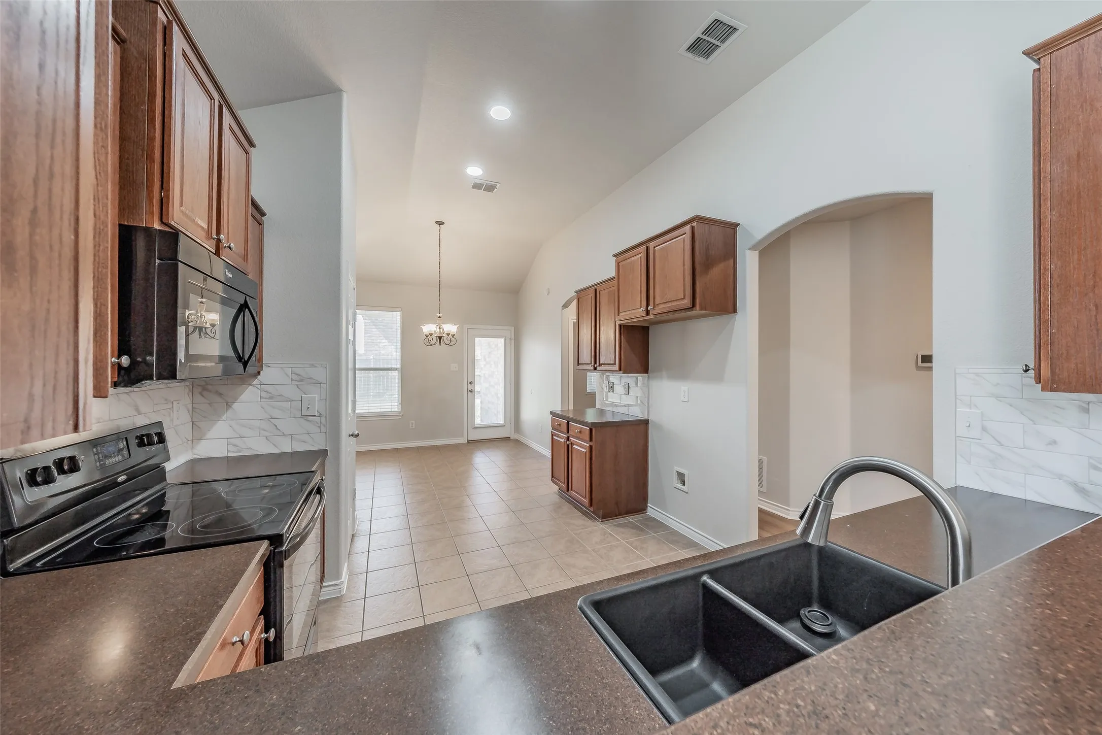 Kitchen featuring wood-finish cabinetry, solid surface countertops, a dual basin sink, integrated appliances, and a tile backsplash