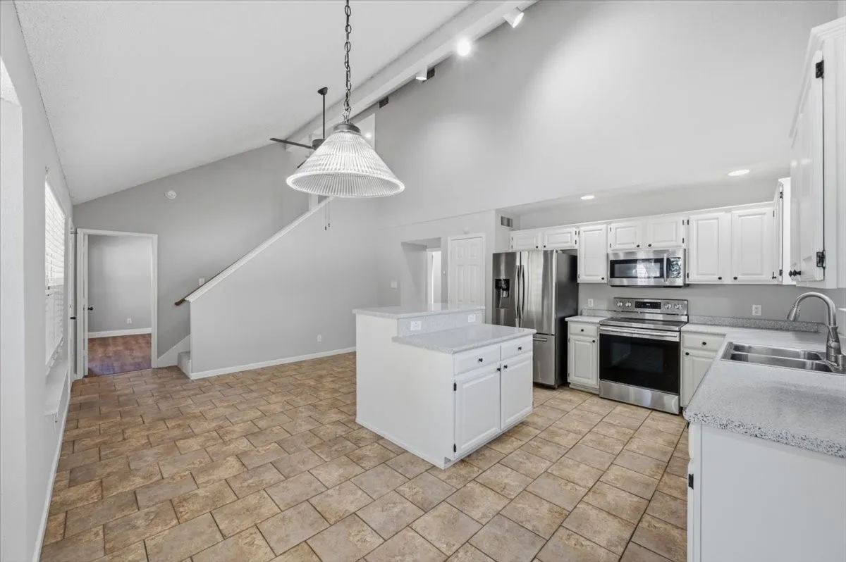 Vaulted ceiling with track lighting, white cabinetry, stainless steel appliances, speckled countertops, and tile flooring
