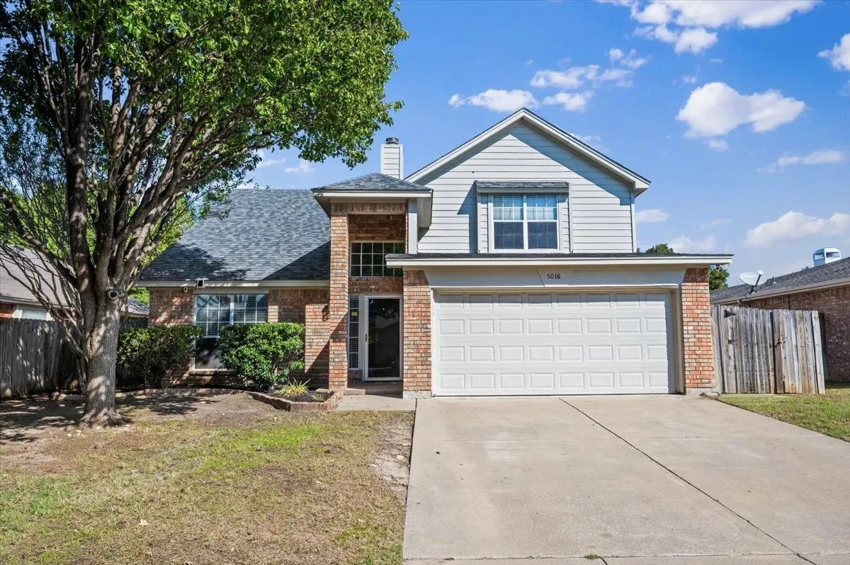 Brick and siding exterior with a two-car garage, established front yard tree, and covered entry
