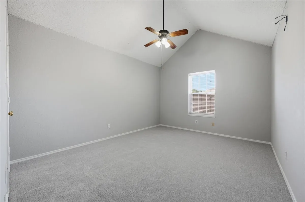 Vaulted ceiling with a ceiling fan, light gray wall finish, gray carpet flooring, and a window with blinds