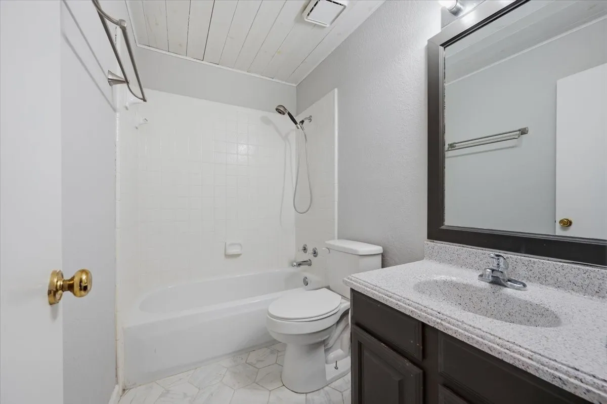 Modern bathroom featuring a white subway tile surround with integrated shower-tub combination, dual vanity with stone-finish countertop and undermount sink, framed mirror with chrome hardware, and ceramic tile flooring
