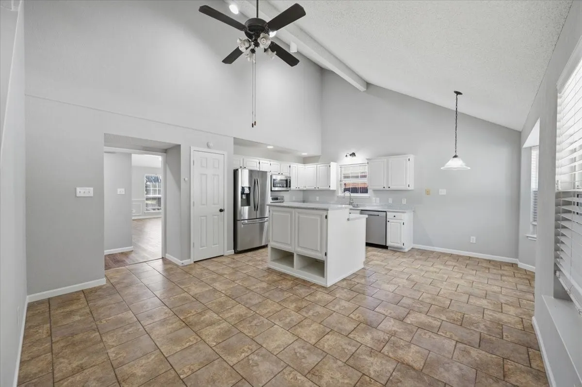 Vaulted ceiling, ceiling fan, white cabinetry, stainless steel appliances, and tile flooring