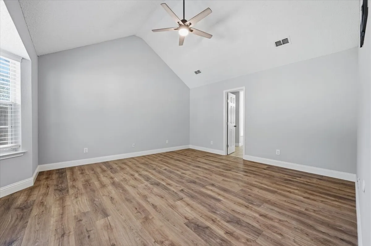 Spacious primary bedroom featuring vaulted ceilings, wood-finish flooring throughout, and abundant natural light from large windows