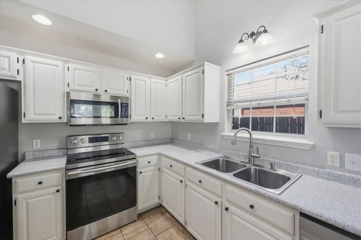 Kitchen featuring white cabinetry, light-toned countertops, a stainless steel oven with an overhead microwave, and a double basin sink with a brushed nickel faucet