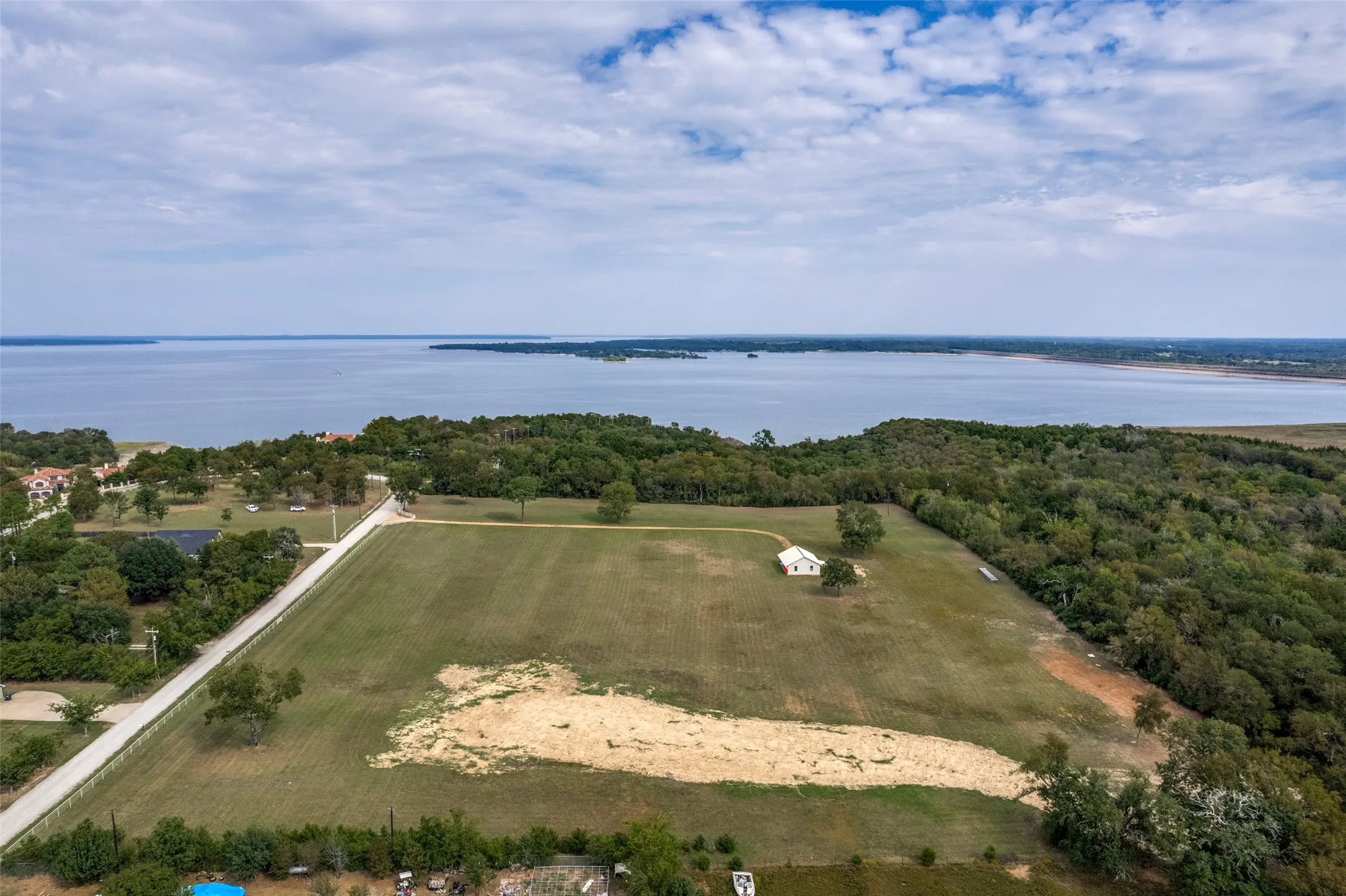Expansive land parcel with a single structure, bordered by mature trees and a substantial body of water