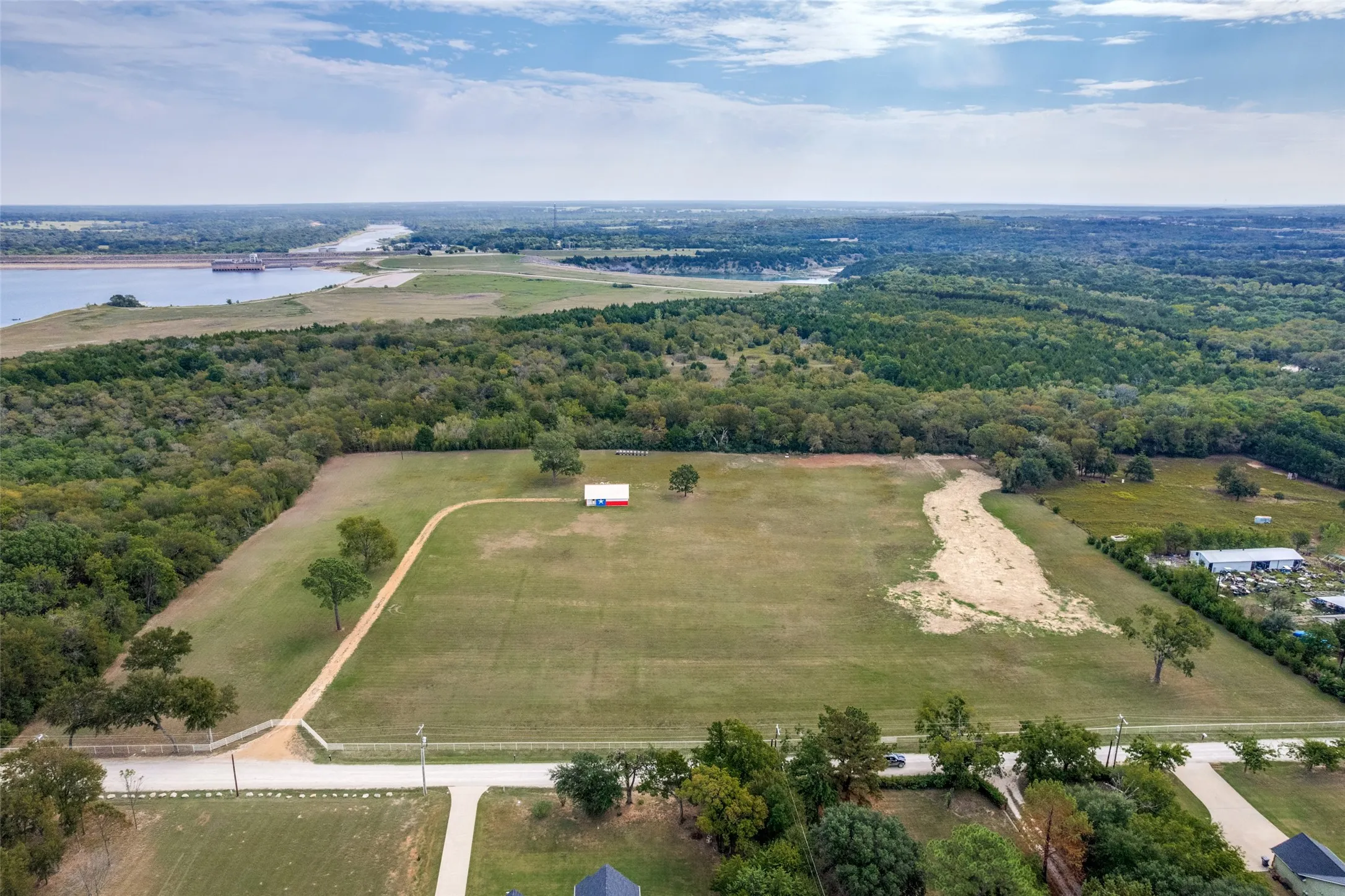 Expansive acreage featuring open pastureland with mature tree lines, a cleared building site with gravel foundation, and direct road frontage