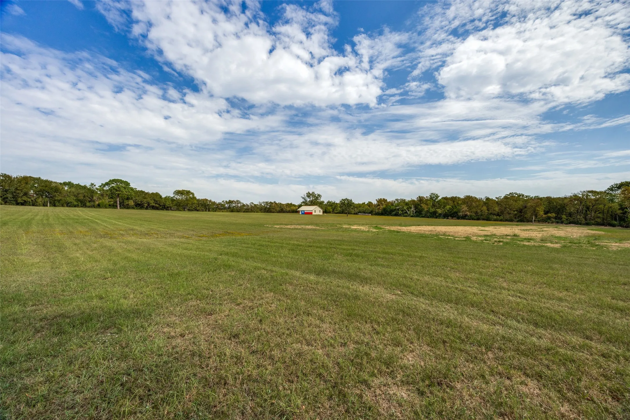 Expansive green field with a distant red and white structure, surrounded by mature trees