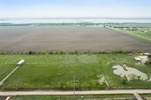 Expansive land parcel featuring a large cultivated field, a pond, and a gravel road leading to structures