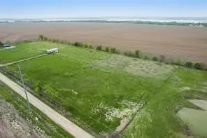 Expansive agricultural land featuring a verdant field, unpaved access road, and water feature