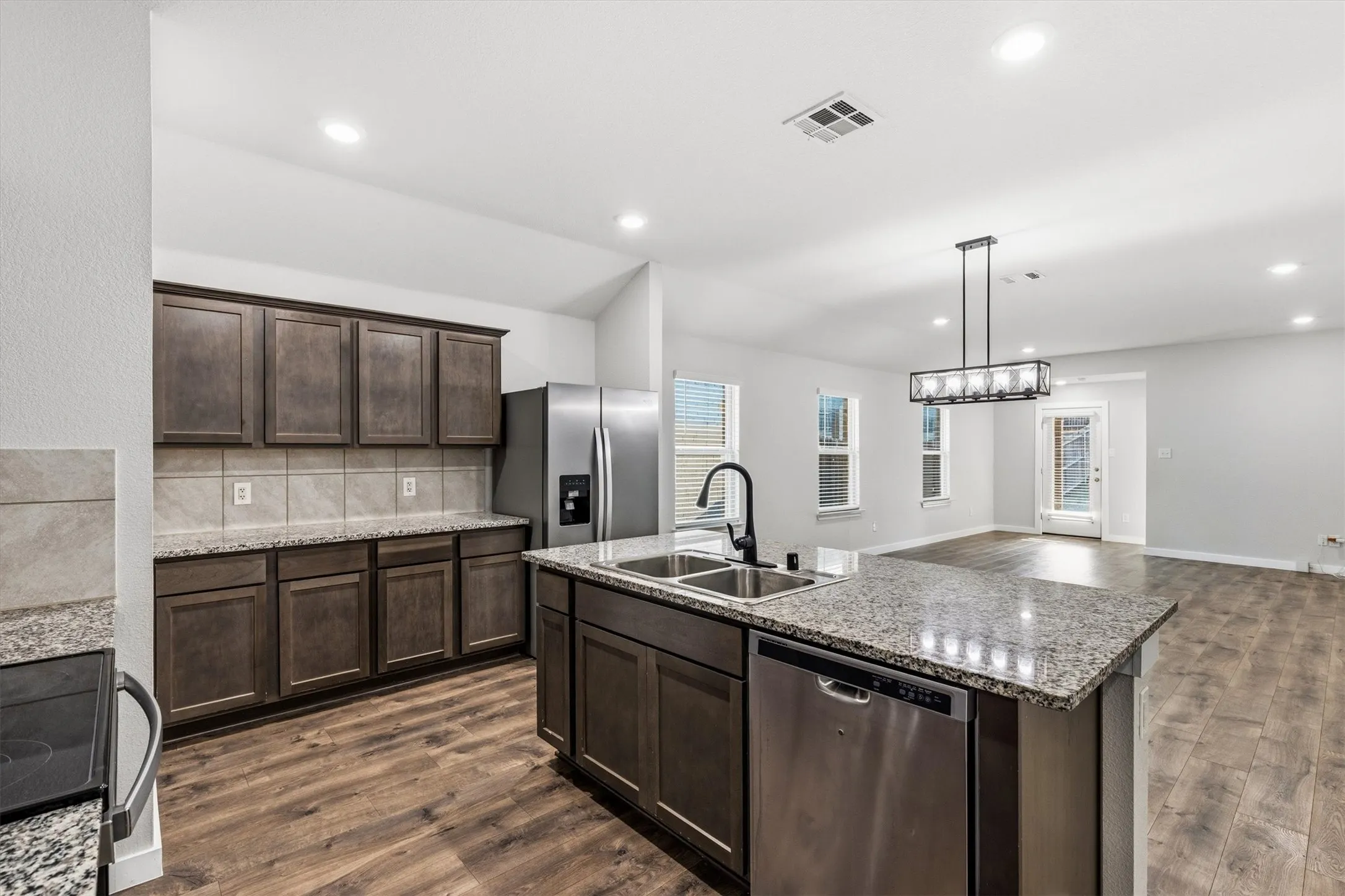 Kitchen featuring wood-finish flooring, dark wood cabinetry, granite countertops, and stainless steel appliances