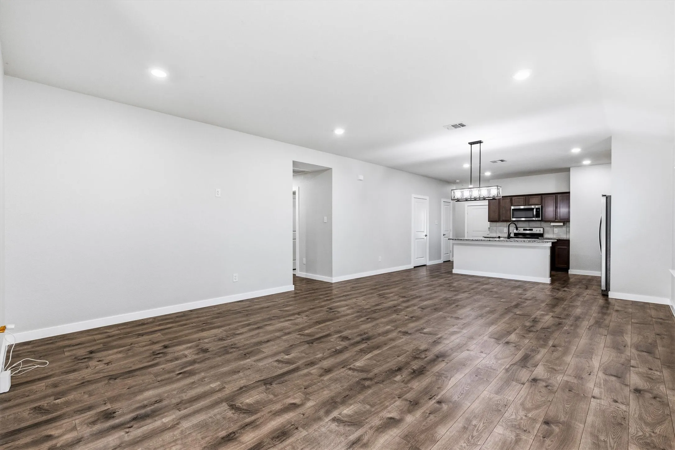 Wood-finish flooring throughout, recessed lighting, and a kitchen featuring dark wood cabinetry, stainless steel appliances, and an island with a breakfast bar