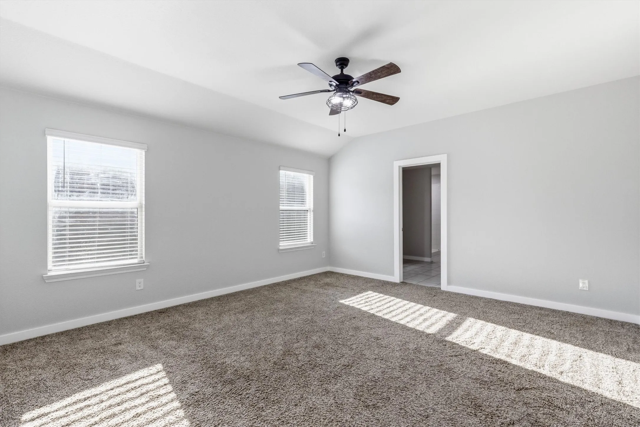 Carpeted flooring, vaulted ceiling, two windows with blinds, recessed lighting on ceiling fan, and painted walls