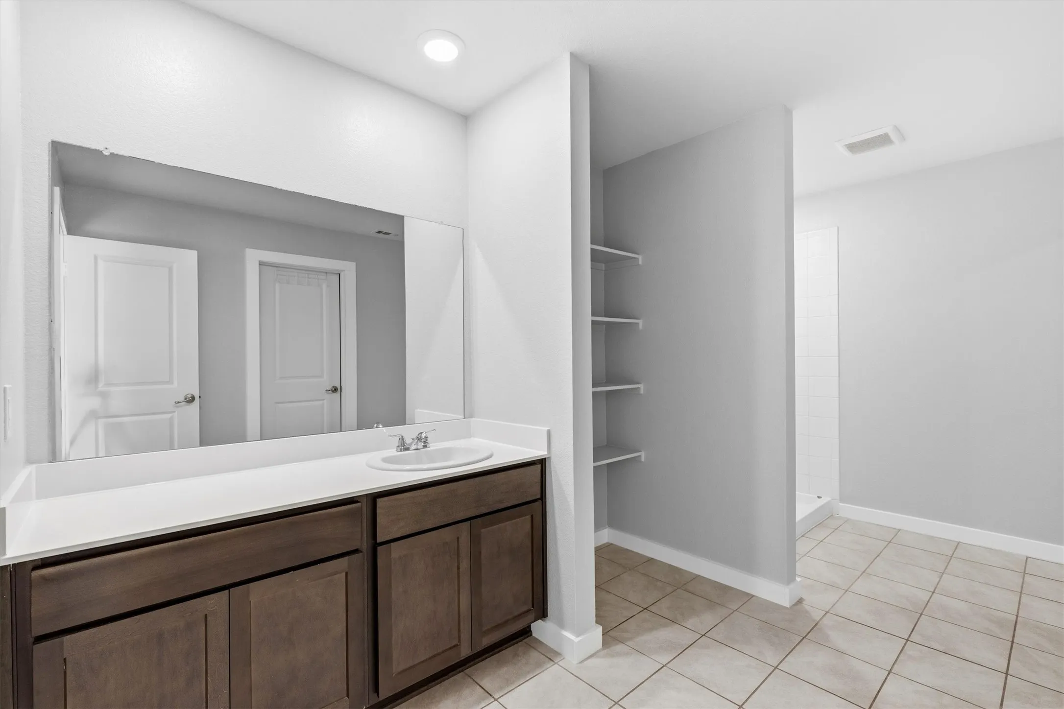 Spa-inspired primary bathroom featuring a dual-sink vanity with wood-finish cabinetry, white quartz countertop, and an oversized framed mirror