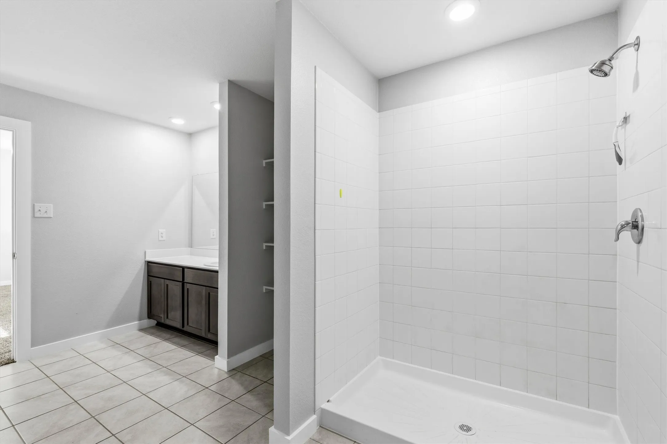 Tiled flooring, built-in shelving, vanity with storage, white countertop, and a tiled shower