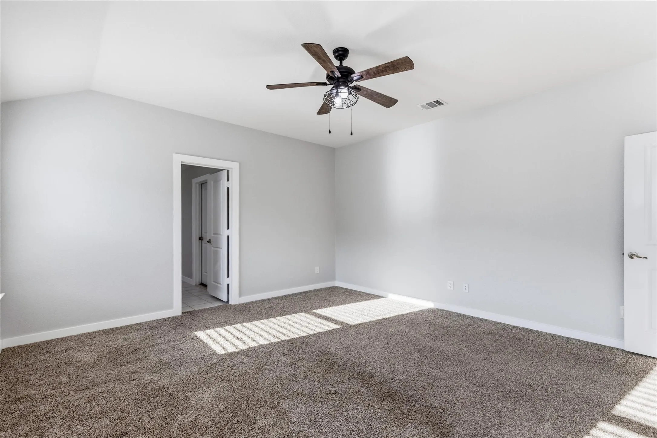 Vaulted ceiling with an installed ceiling fan, light gray wall paint, and gray carpet