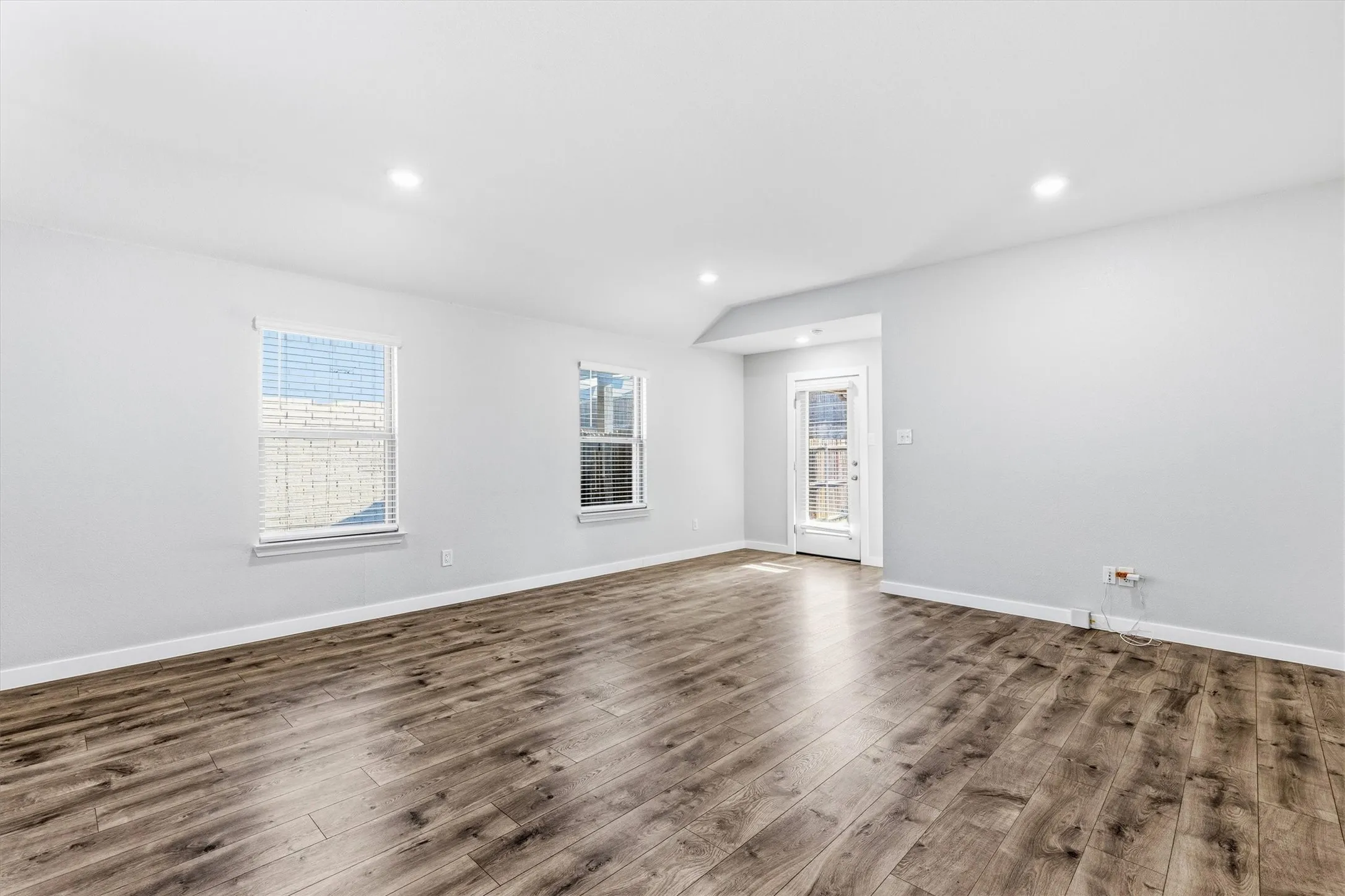 Spacious room featuring wood-finish flooring, recessed lighting, and multiple windows with blinds
