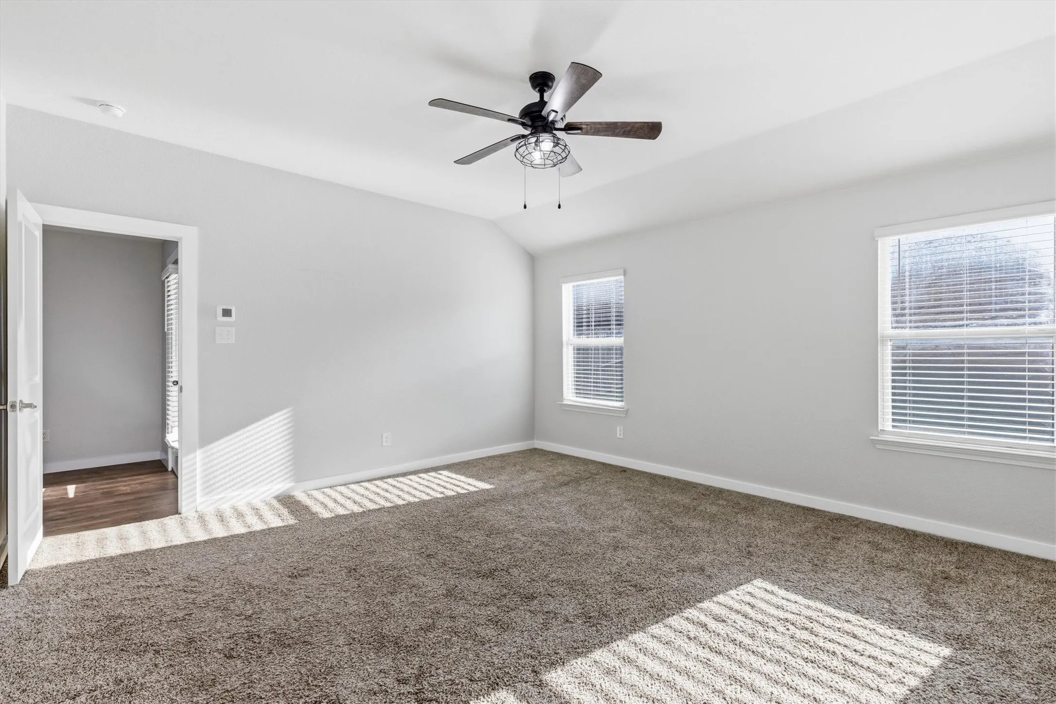 Vaulted ceiling with an attached ceiling fan, dual windows with blinds, and neutral carpeting