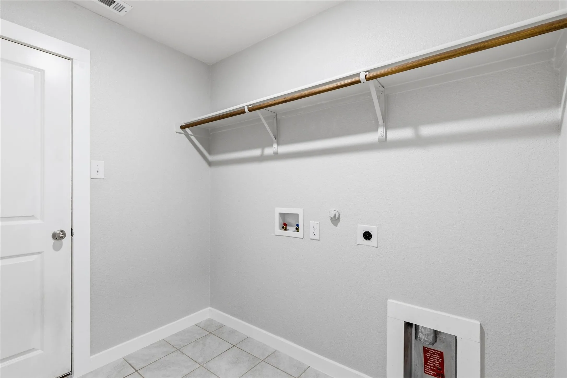 Utility room featuring a built-in hanging rod, wall-mounted shelving, and tile flooring