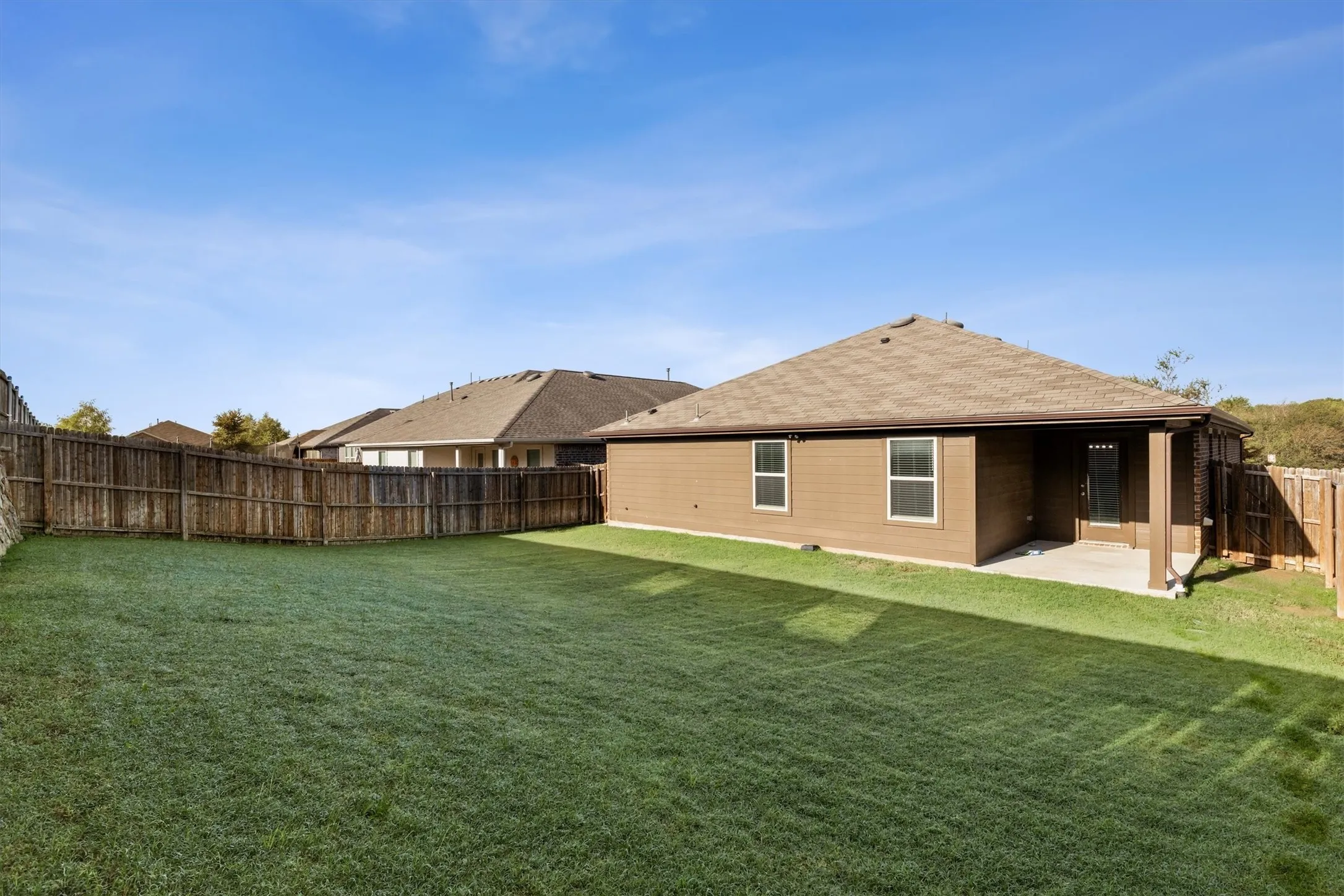 Expansive fenced backyard with a manicured lawn, covered patio, and brown siding