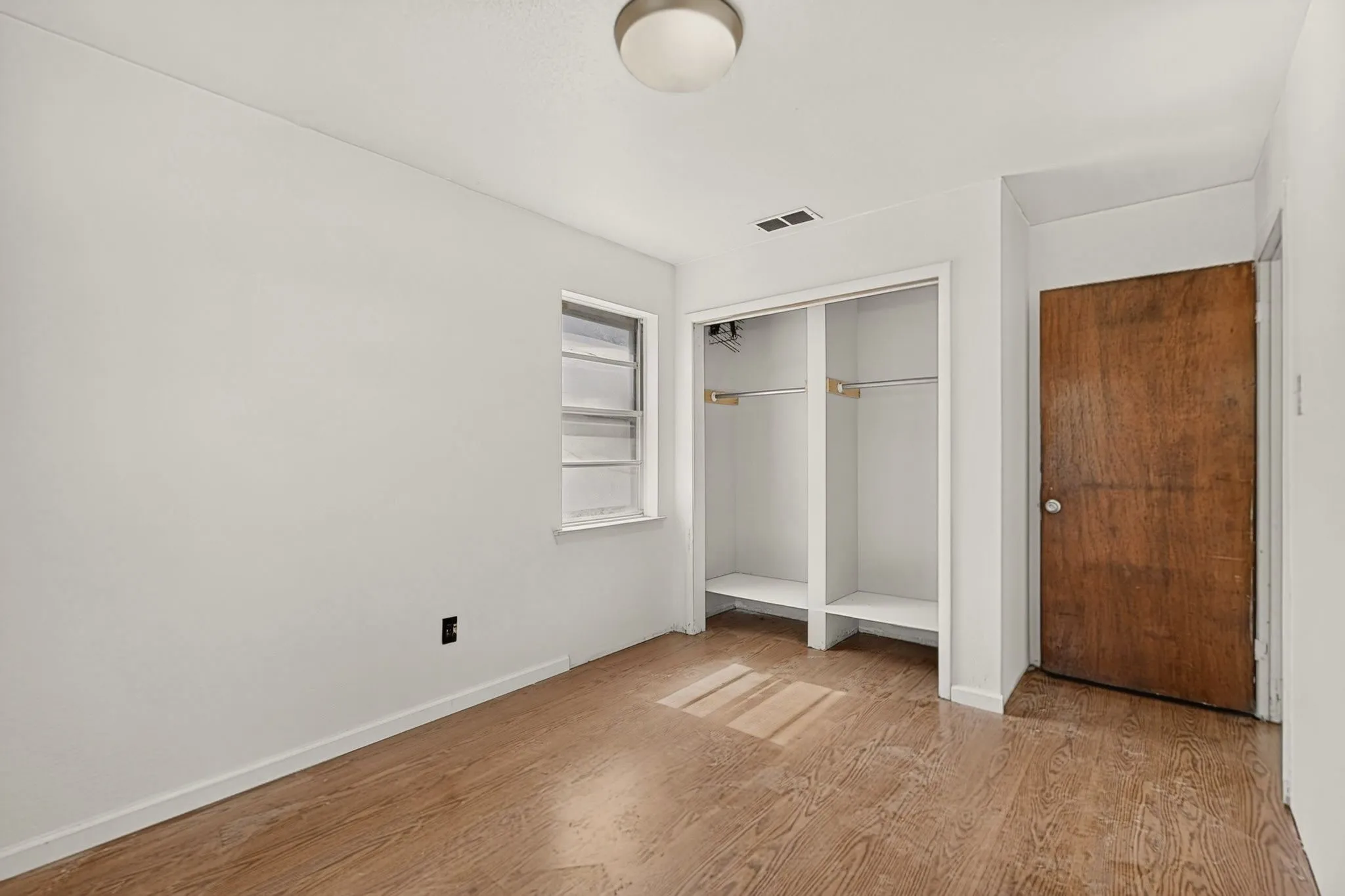 Wood-finish flooring with a built-in closet featuring shelving and hanging rods