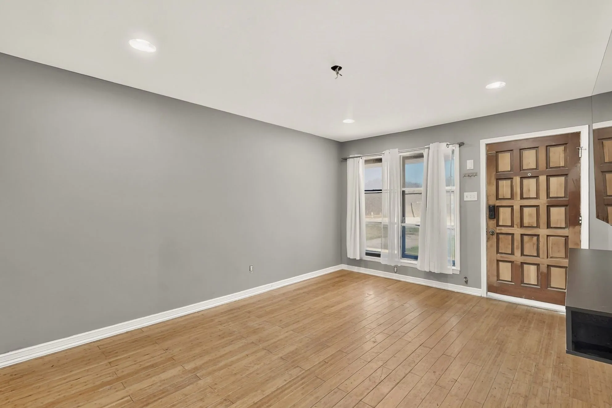 Wood-finish flooring, recessed ceiling lighting, textured entry door, and multiple windows