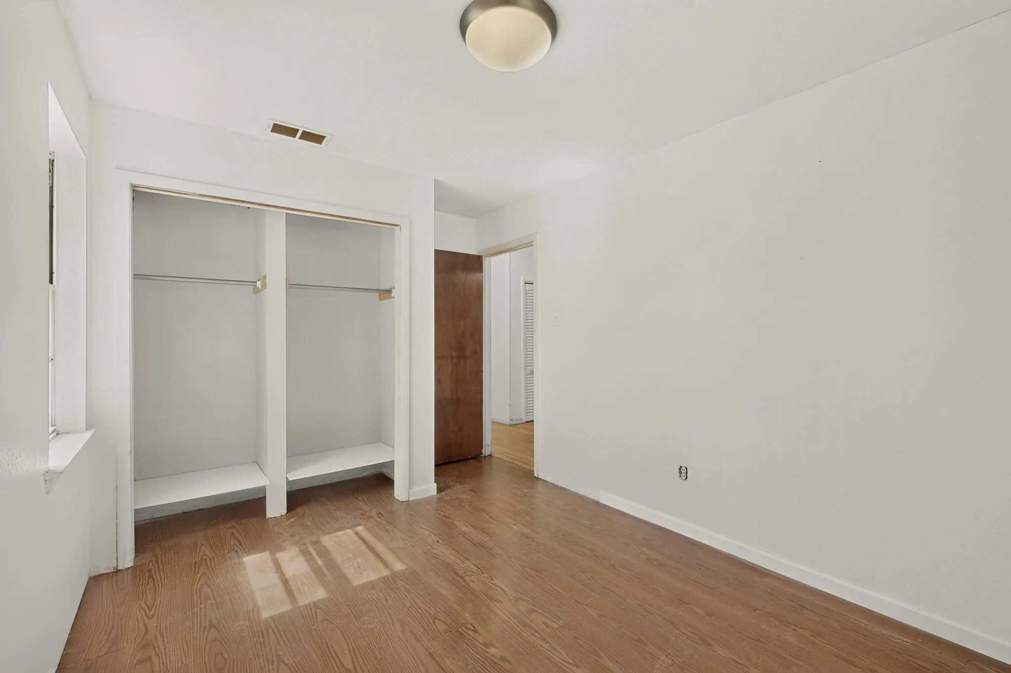 Wood-finish flooring throughout, white painted walls, and a built-in closet with shelving and hanging rods