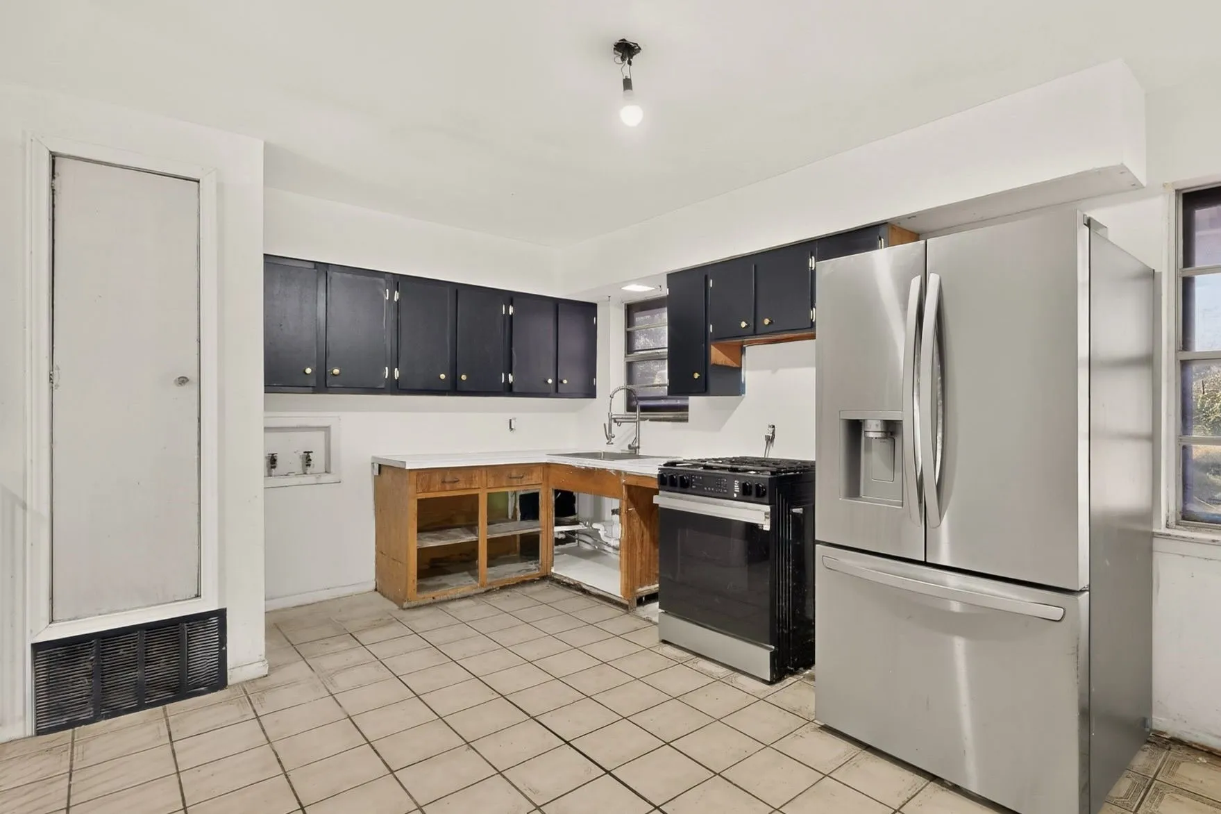 Stainless steel refrigerator and gas range with tile flooring, dark cabinetry, and a single basin sink